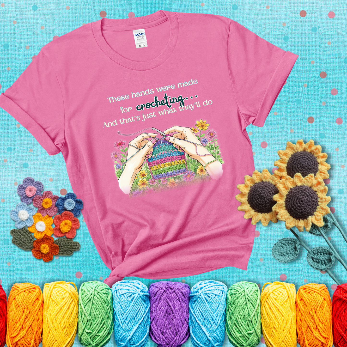 Illustration of two hands crocheting a rainbow swatch, surrounded by vibrant flowers with the phrase “These hands were made for crocheting… and that’s just what they’ll do,” showing a pink tee with a teal sunflower background