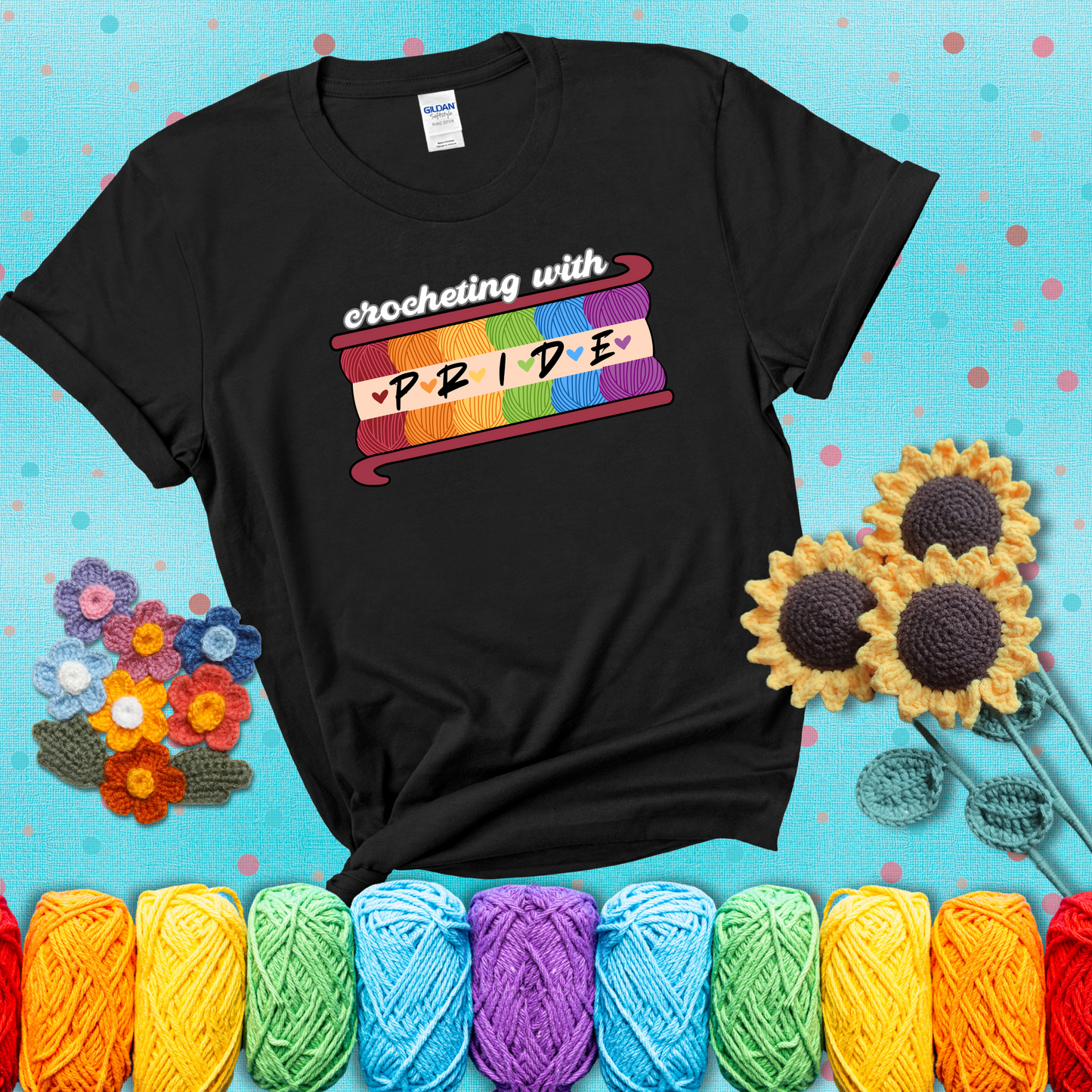 Yarn skeins in rainbow colors stacked in a hook shape. Text reads “Crocheting With Pride” showing a black tee with a teal sunflower background