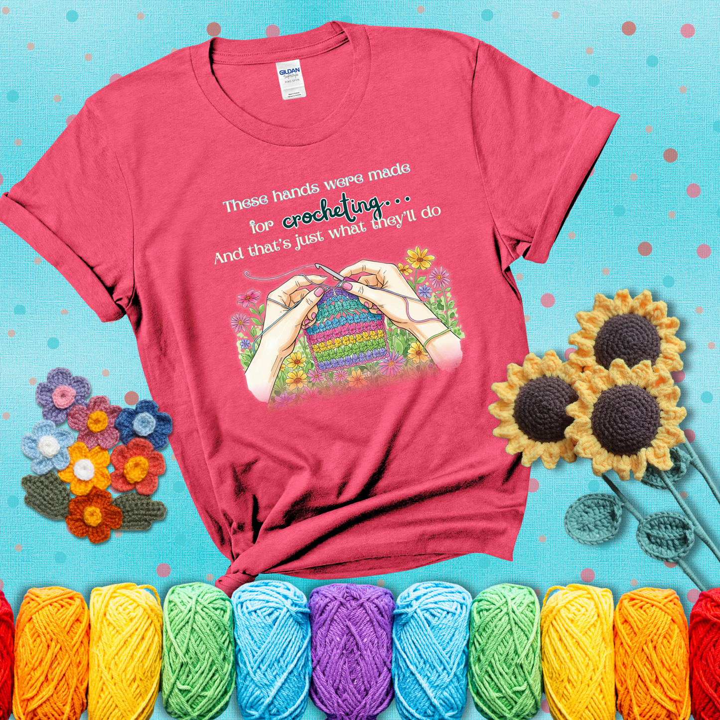 Illustration of two hands crocheting a rainbow swatch, surrounded by vibrant flowers with the phrase “These hands were made for crocheting… and that’s just what they’ll do,” showing a light red tee with a teal sunflower background