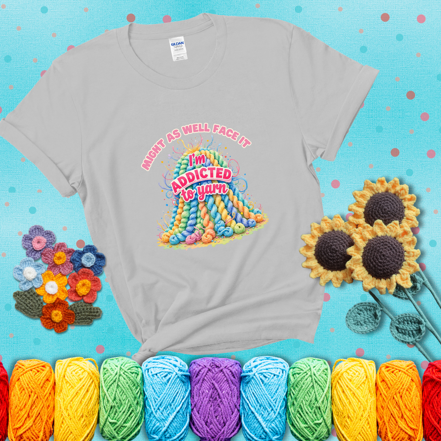Colorful mountain of pastel yarn hanks with the phrase “Might as well face it, I’m addicted to yarn” in playful pink and red lettering showing a light grey tee with a teal sunflower background