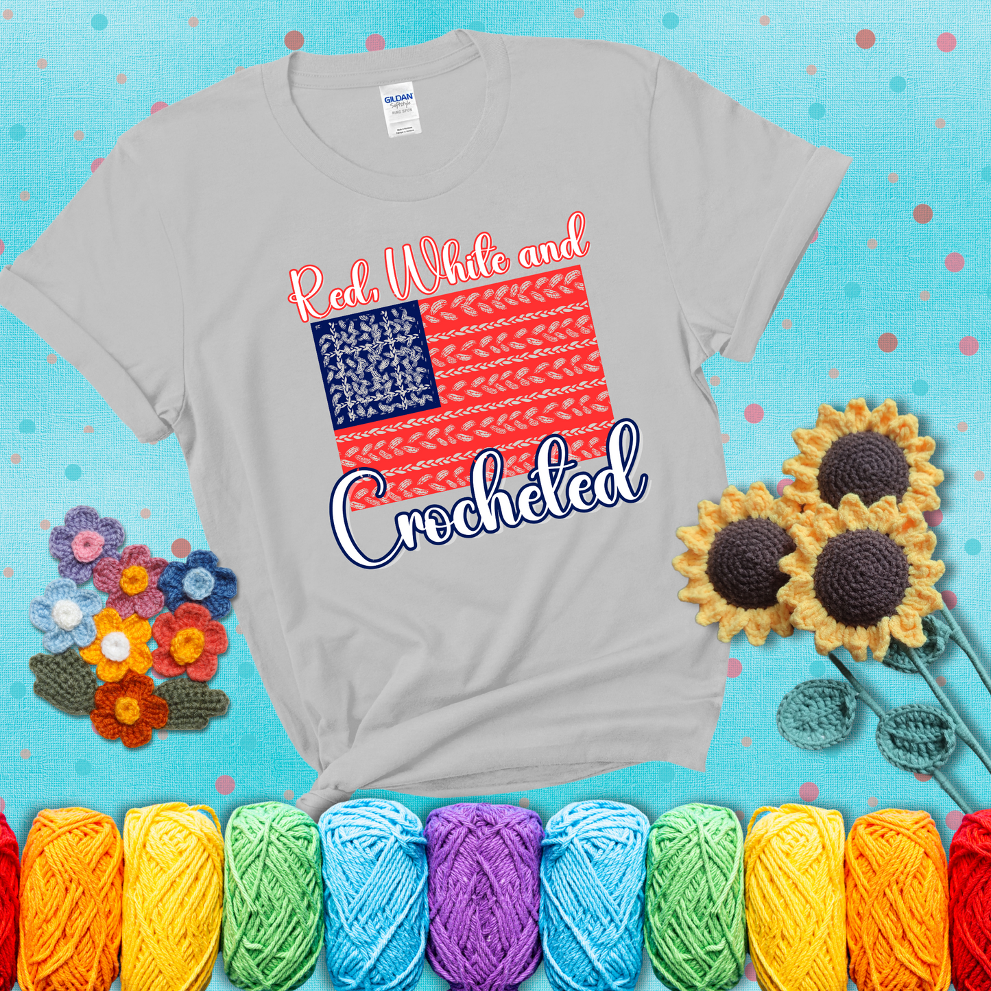 Patriotic crochet-themed American flag design with red and white yarn stitches forming the stripes and blue and white stitches as stars, showing a light grey tee with a teal sunflower background