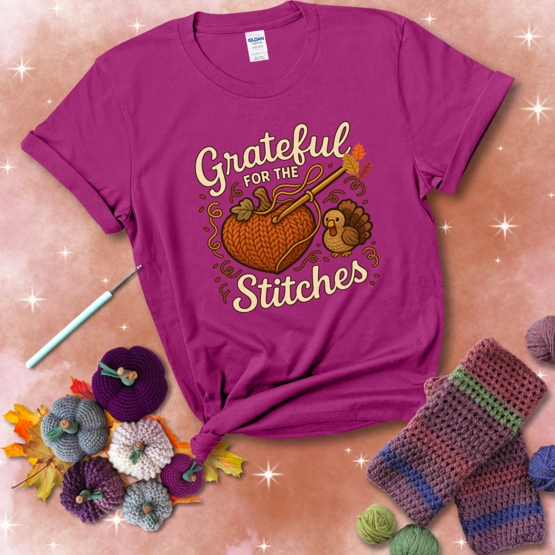 A cozy fall scene with a crochet hook stitching a heart-shaped pumpkin, surrounded by yarn and a small turkey, showing a magenta tee with a festive Fall background