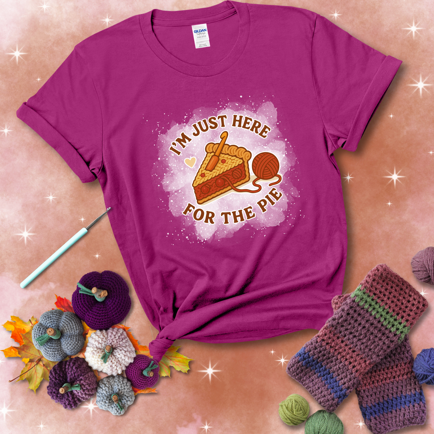 A slice of cherry pie with a crochet hook tucked in the filling and yarn trailing out, blending baking with crochet fun, showing a magenta tee with a festive Fall background
