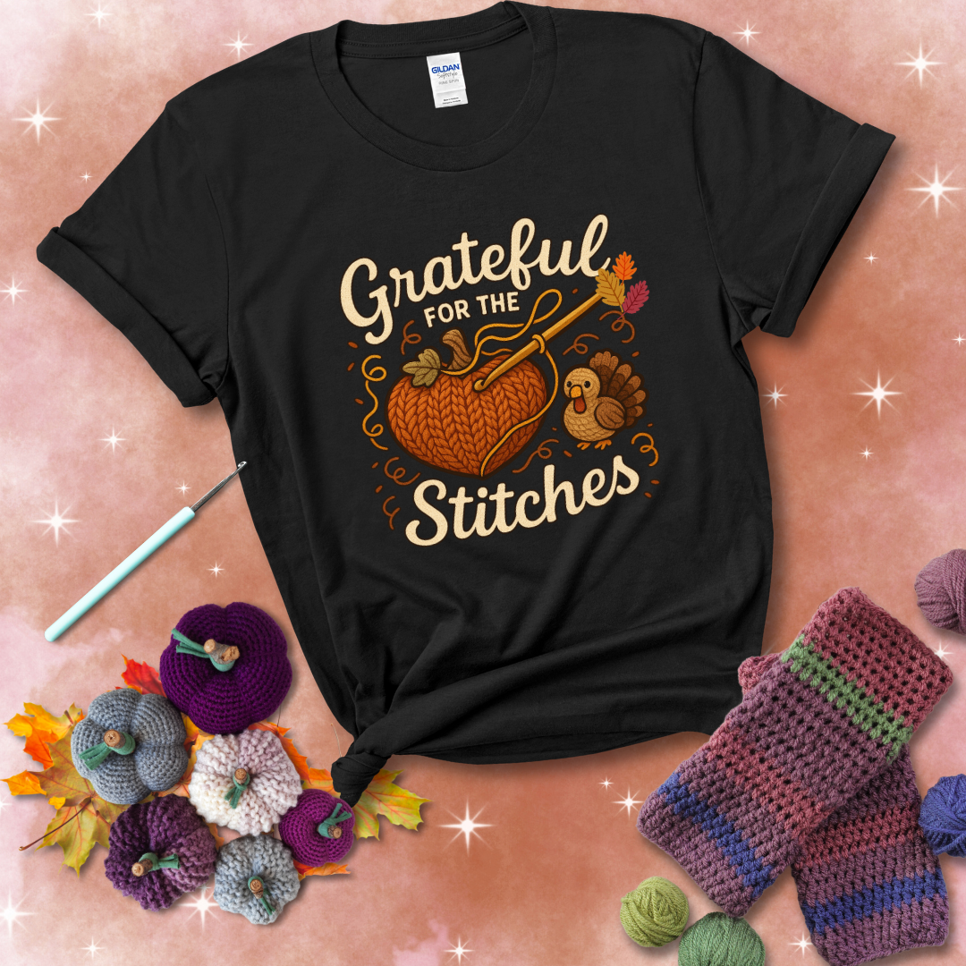 A cozy fall scene with a crochet hook stitching a heart-shaped pumpkin, surrounded by yarn and a small turkey, showing a black tee with a festive Fall background