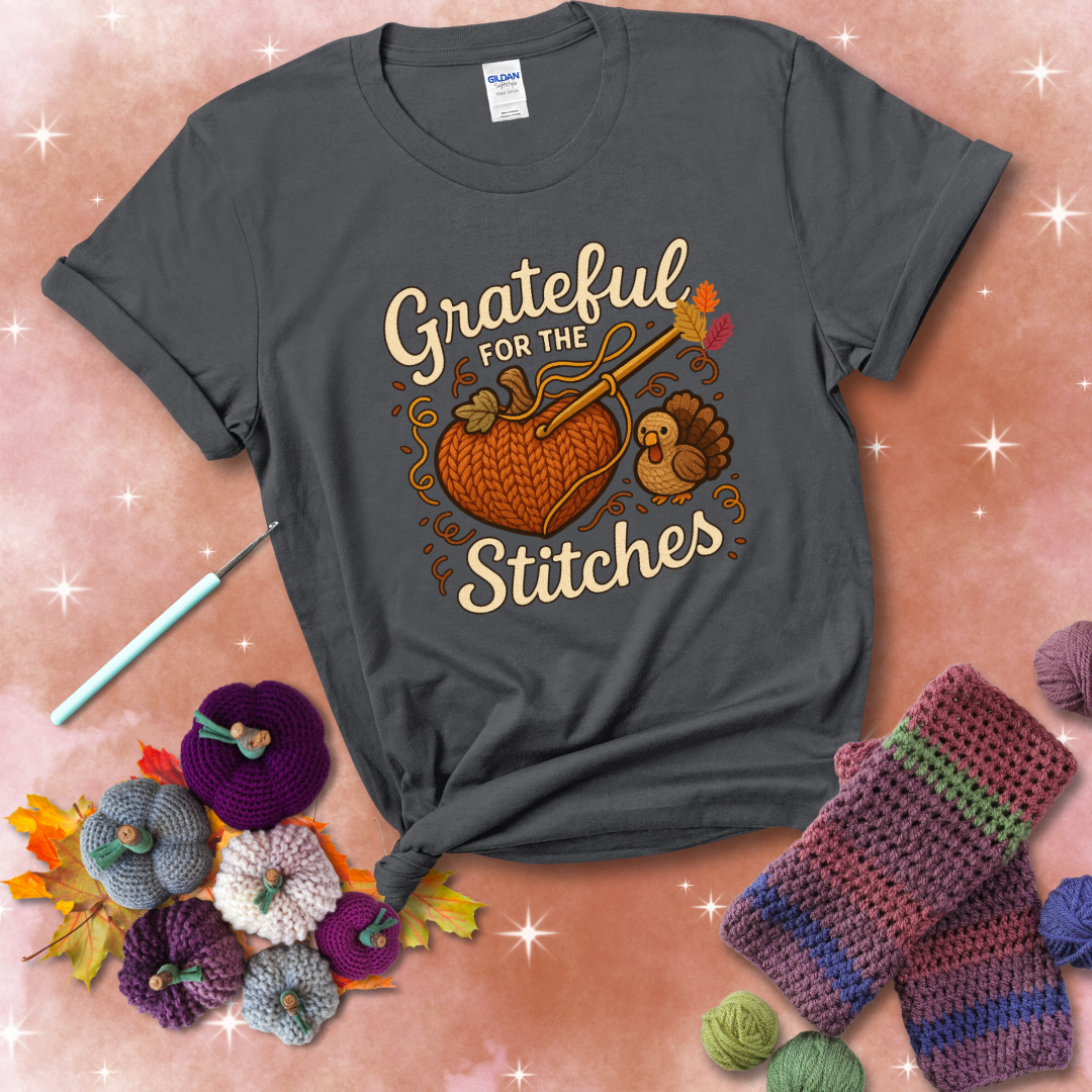 A cozy fall scene with a crochet hook stitching a heart-shaped pumpkin, surrounded by yarn and a small turkey, showing a dark grey tee with a festive Fall background