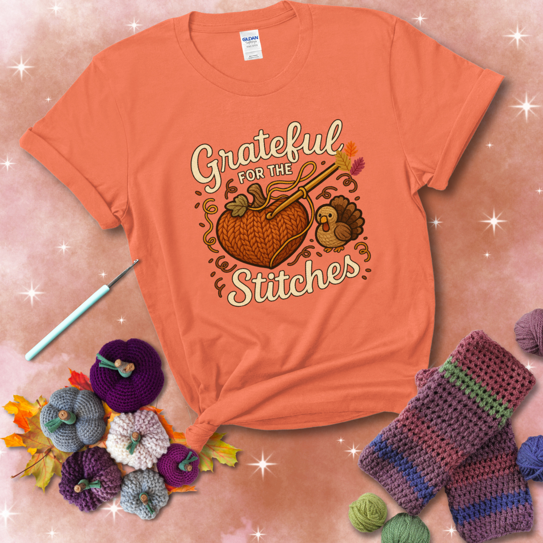 A cozy fall scene with a crochet hook stitching a heart-shaped pumpkin, surrounded by yarn and a small turkey, showing a light orange tee with a festive Fall background