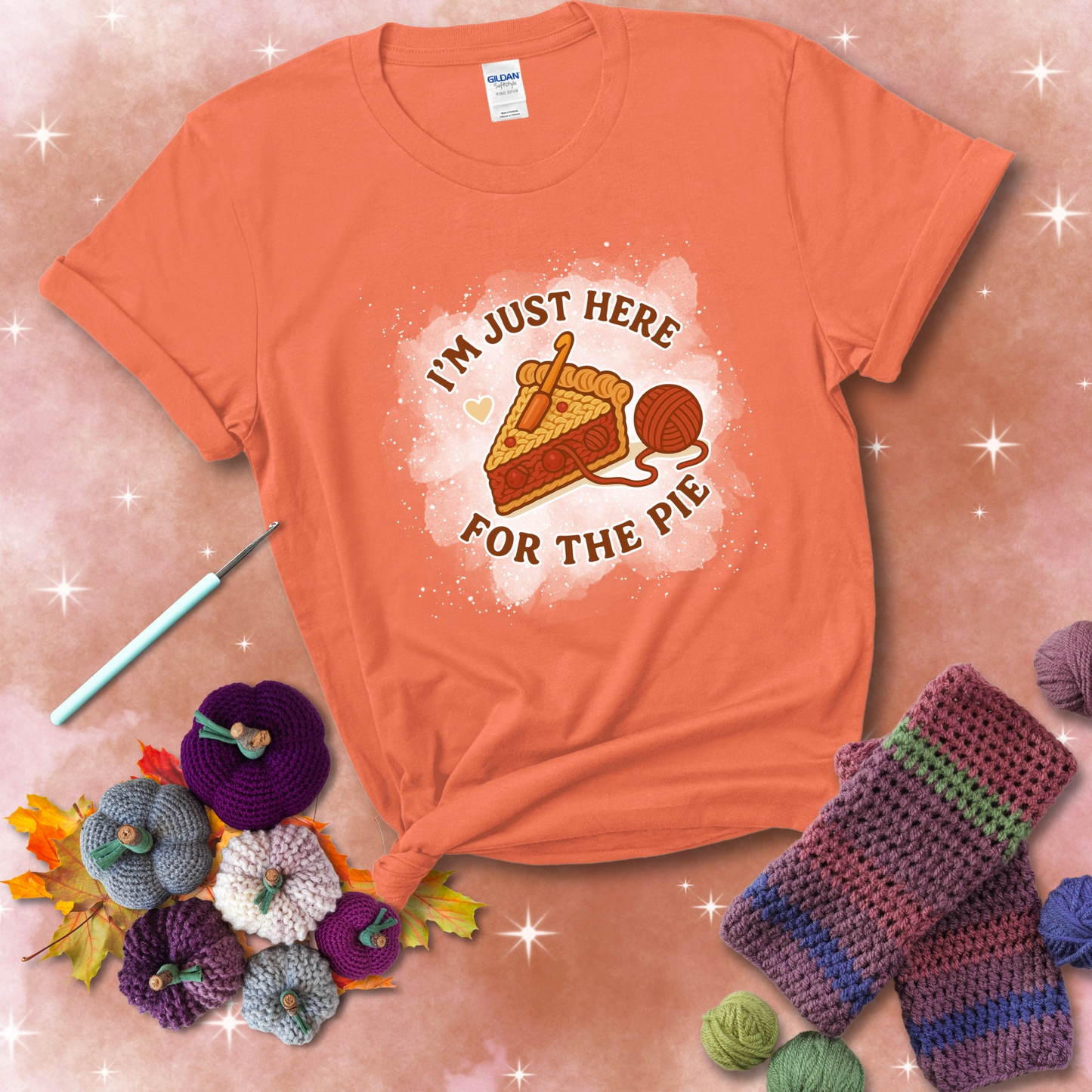 A slice of cherry pie with a crochet hook tucked in the filling and yarn trailing out, blending baking with crochet fun, showing a light orange tee with a festive Fall background