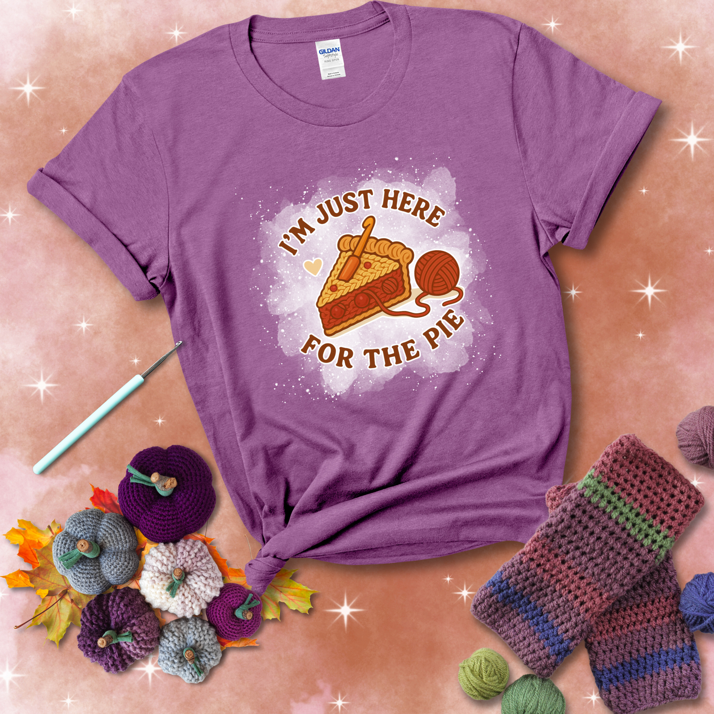 A slice of cherry pie with a crochet hook tucked in the filling and yarn trailing out, blending baking with crochet fun, showing a light purple tee with a festive Fall background