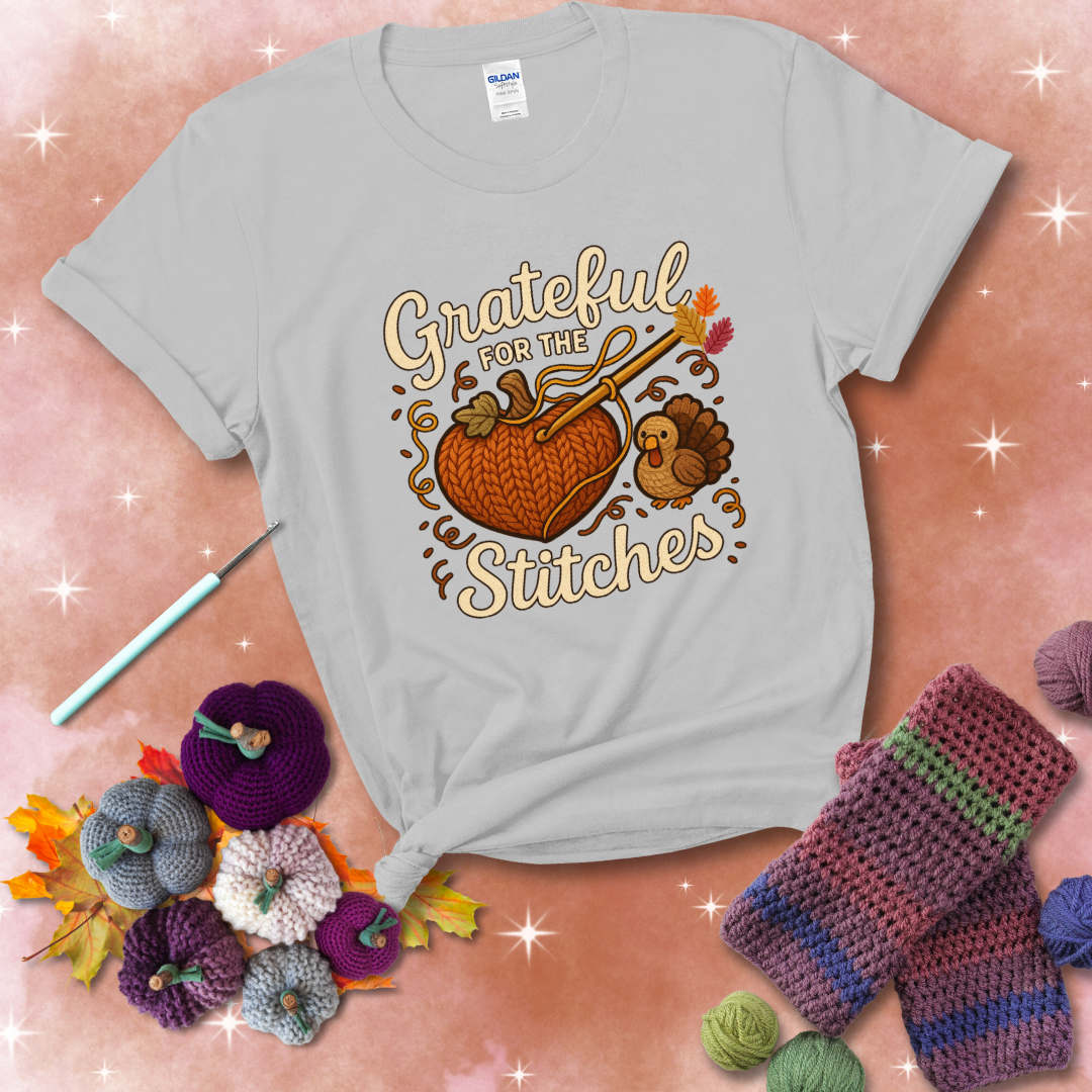 A cozy fall scene with a crochet hook stitching a heart-shaped pumpkin, surrounded by yarn and a small turkey, showing a light grey tee with a festive Fall background