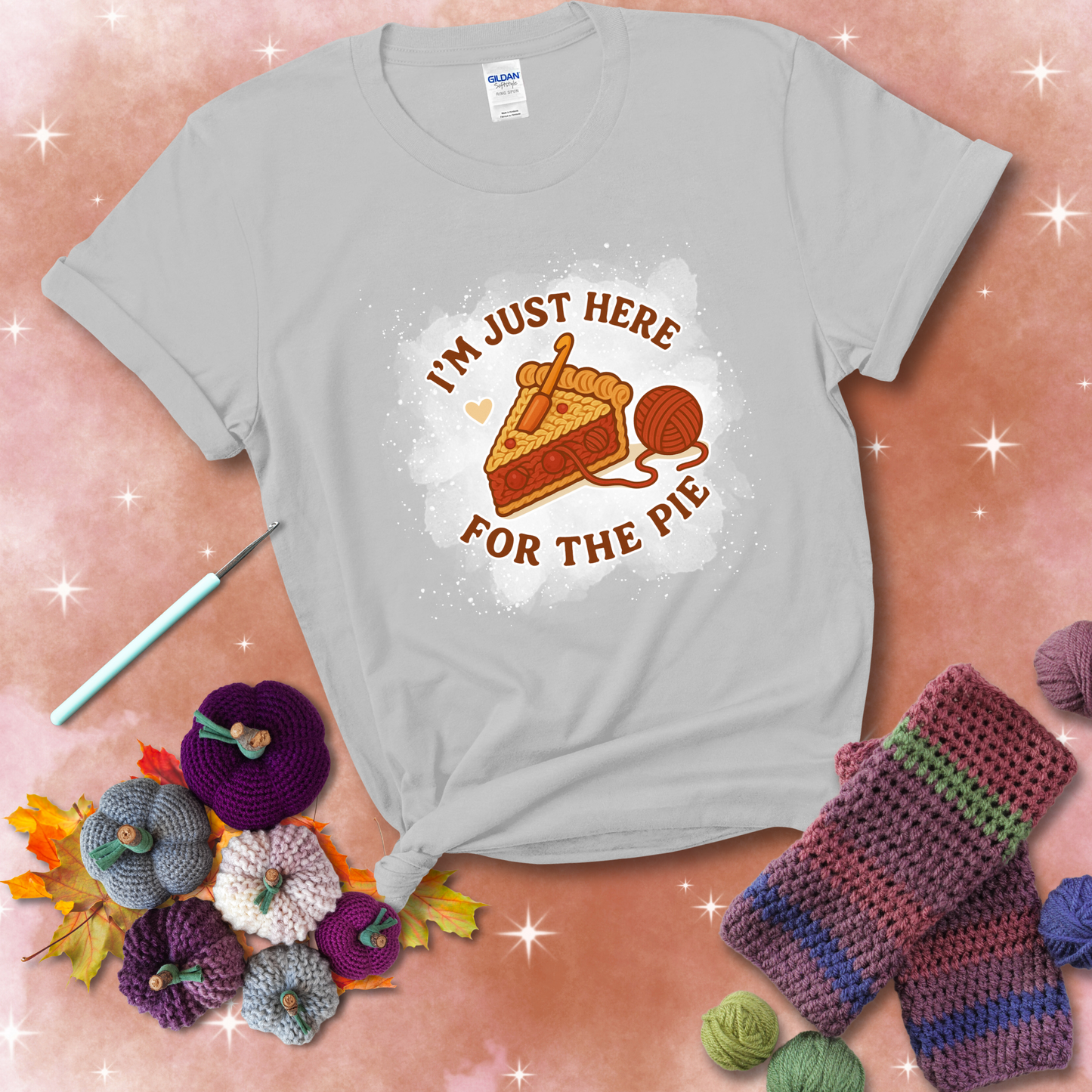 A slice of cherry pie with a crochet hook tucked in the filling and yarn trailing out, blending baking with crochet fun, showing a light grey tee with a festive Fall background