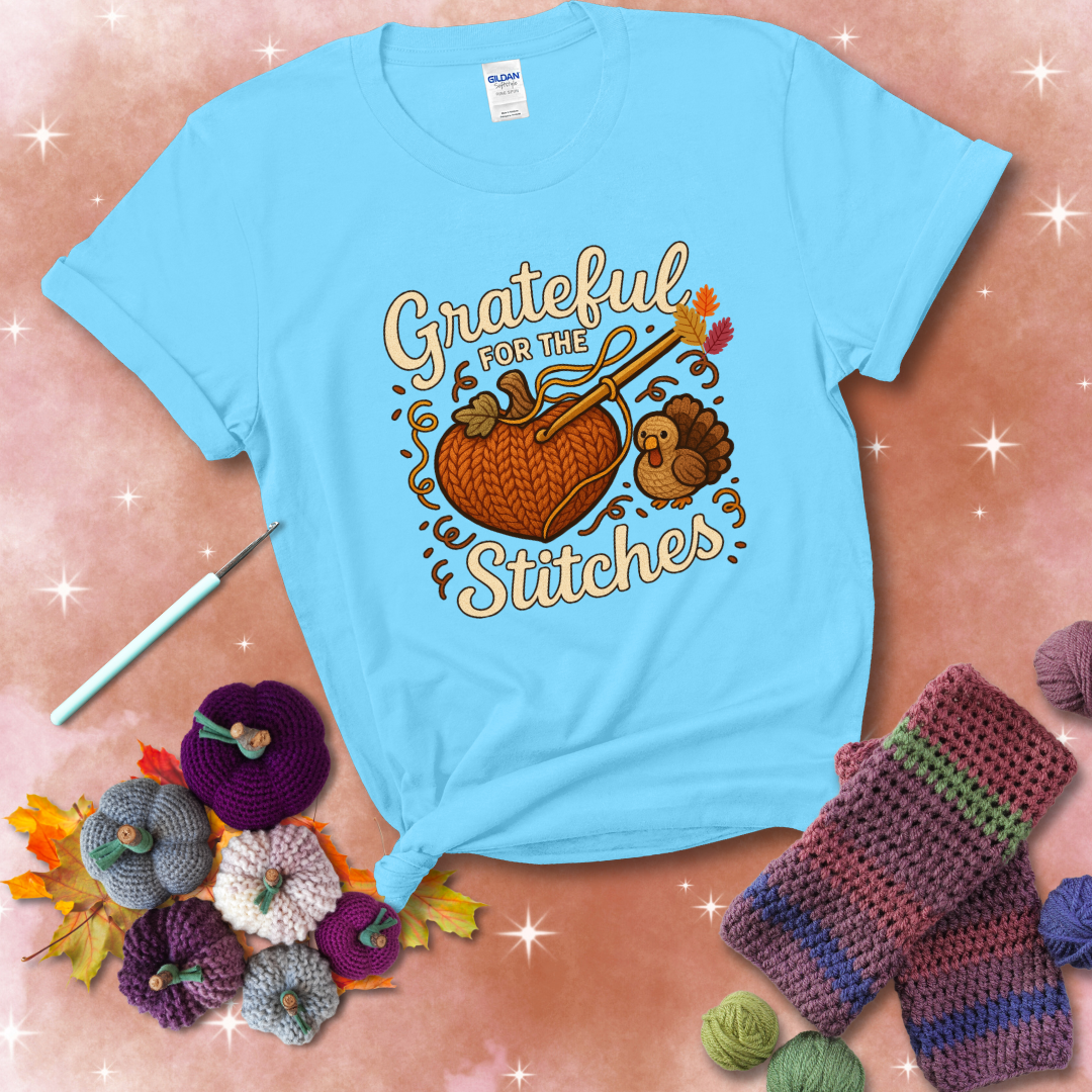 A cozy fall scene with a crochet hook stitching a heart-shaped pumpkin, surrounded by yarn and a small turkey, showing a light blue tee with a festive Fall background