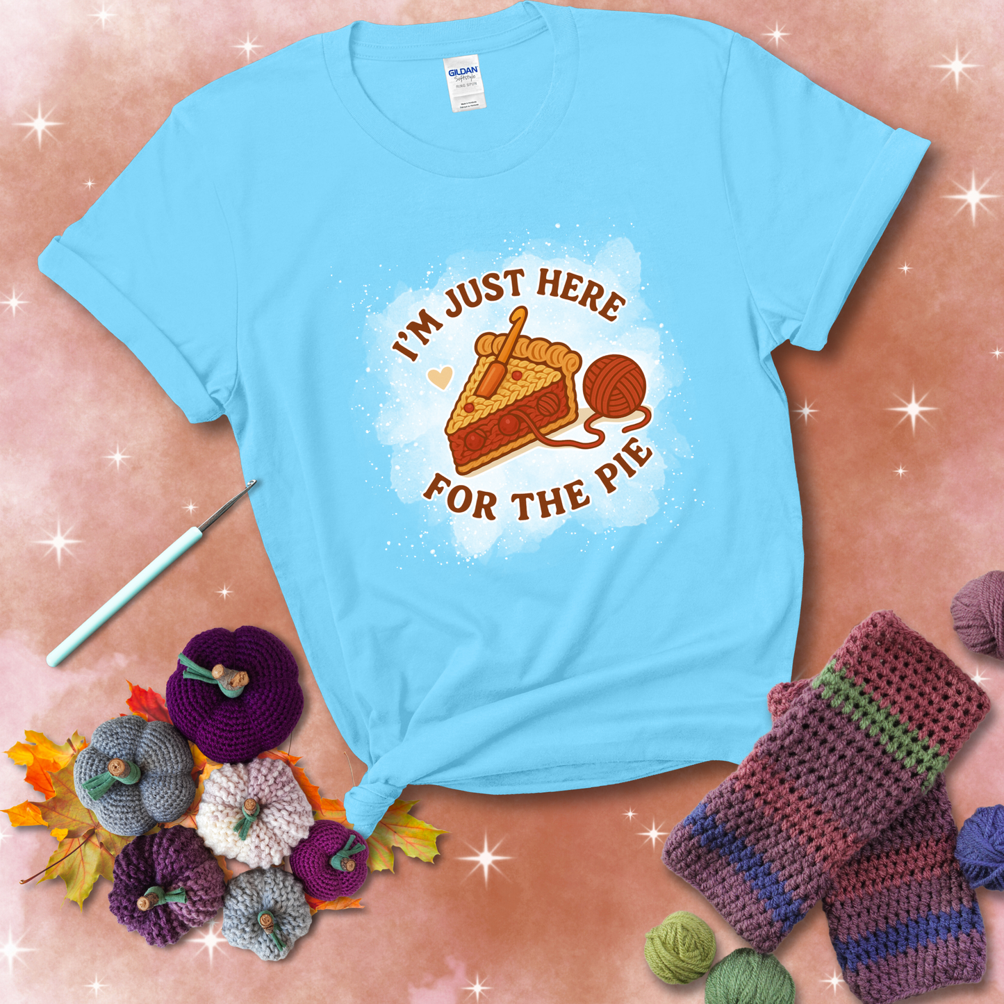 A slice of cherry pie with a crochet hook tucked in the filling and yarn trailing out, blending baking with crochet fun, showing a light blue tee with a festive Fall background