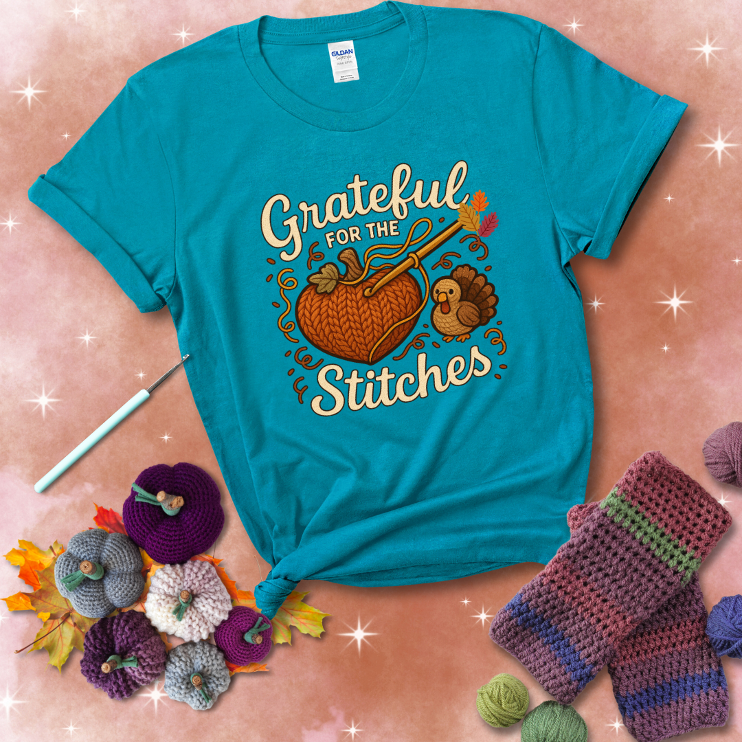 A cozy fall scene with a crochet hook stitching a heart-shaped pumpkin, surrounded by yarn and a small turkey, showing a blue-green tee with a festive Fall background