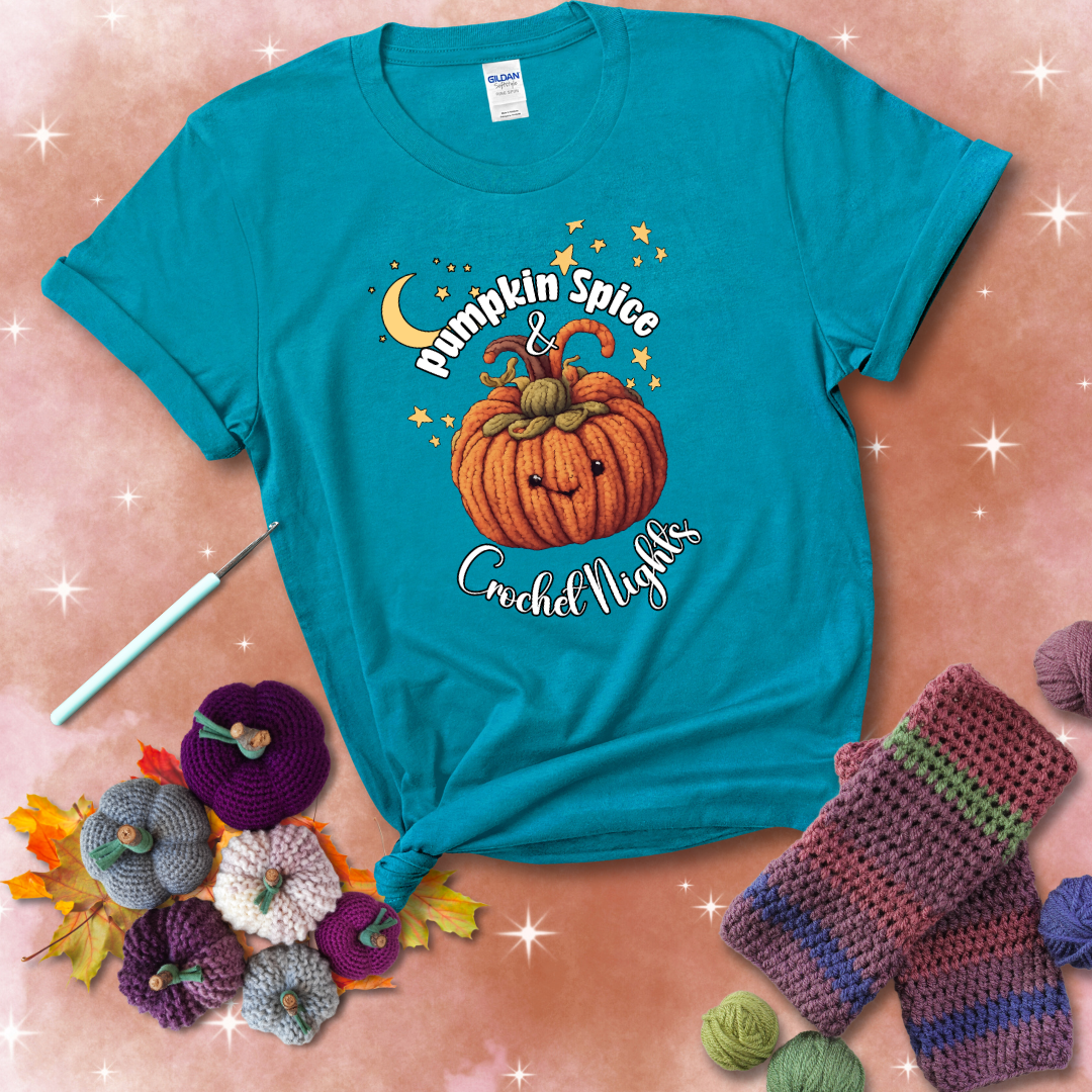 Smiling pumpkin crocheted with yarn texture, surrounded by stars and a crescent moon. Text reads “Pumpkin Spice & Crochet Nights” showing a blue-green tee with a festive Fall background