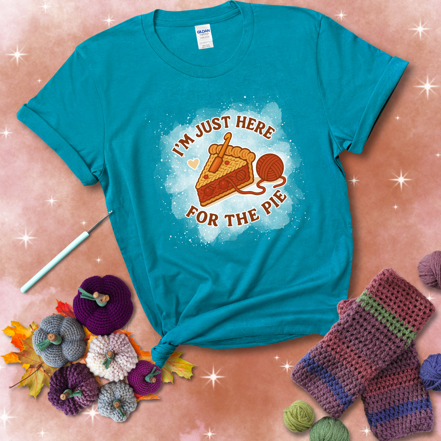 A slice of cherry pie with a crochet hook tucked in the filling and yarn trailing out, blending baking with crochet fun, showing a blue-green tee with a festive Fall background