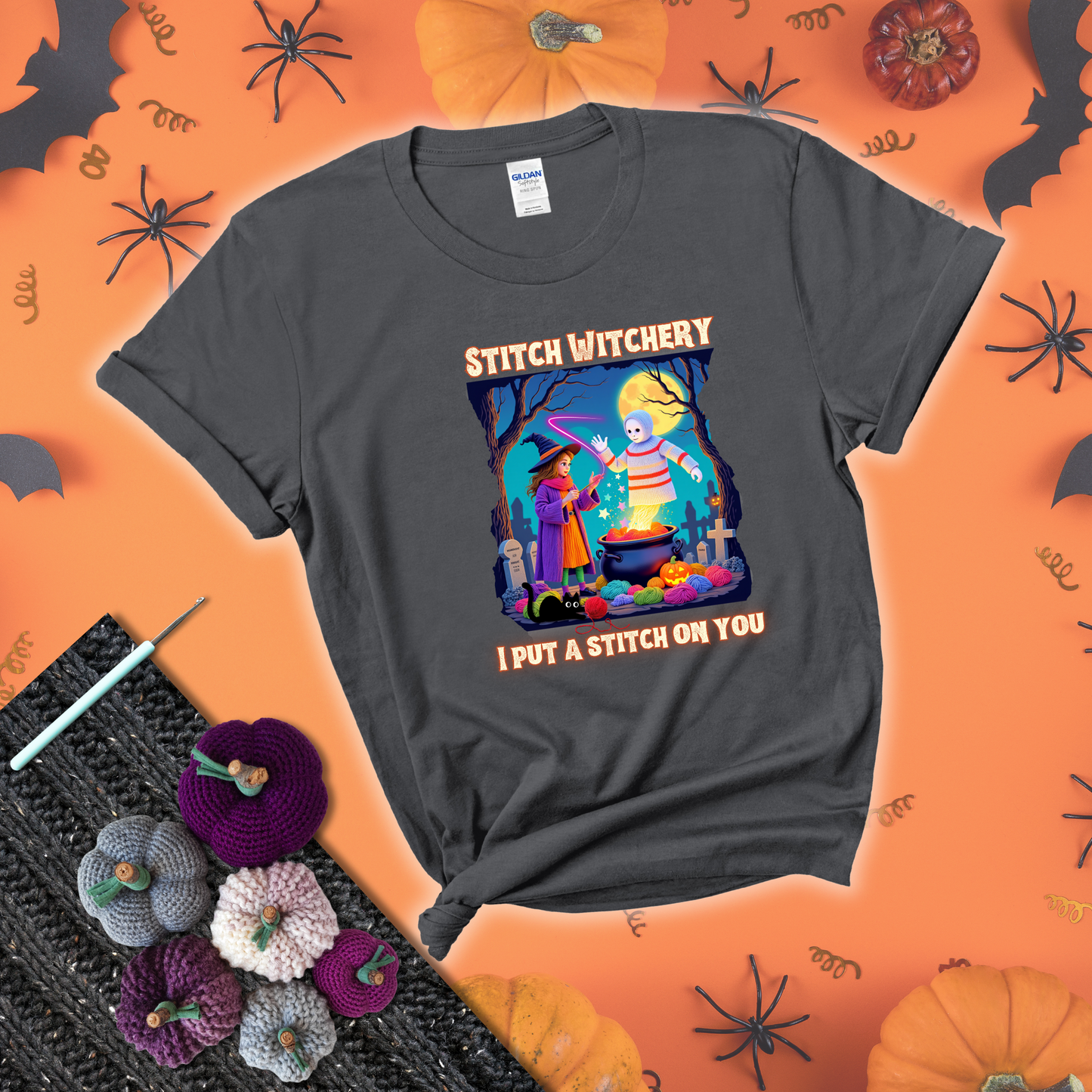 A Halloween scene with a young witch casting a yarn spell from a cauldron onto a floating crochet-ghost figure, under the phrase “I Put a Stitch on You” showing a dark grey tee with a festive Halloween background