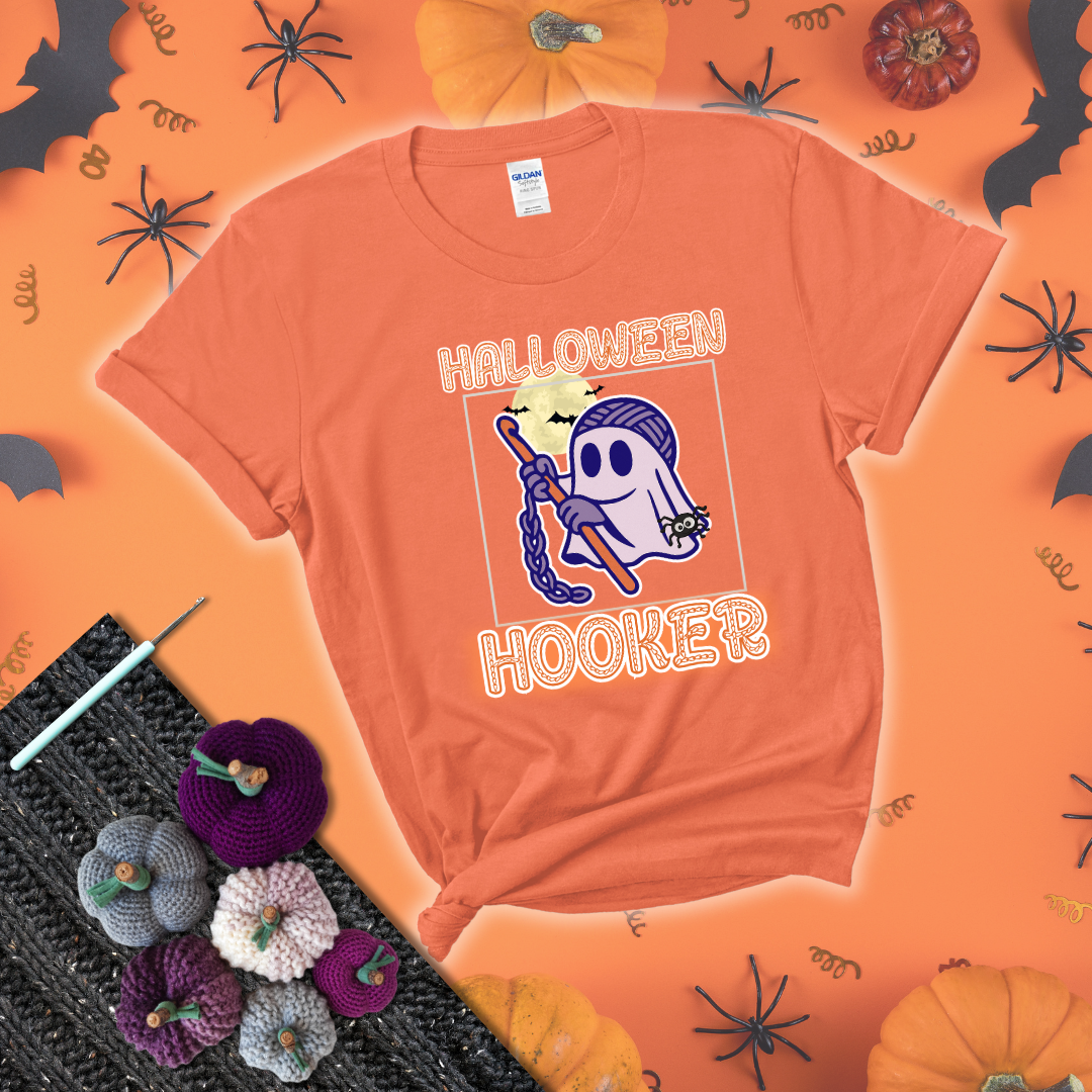 Cartoon ghost crocheter with a yarn ball head, crochet hook, bats, and text “Halloween Hooker,” a fun spooky tee for yarn lovers showing a light orange tee with a festive Halloween background
