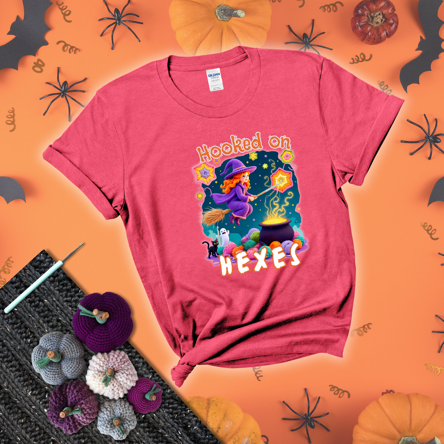 Witchy vibe with stars, hexagons, and a crochet hook. Text reads: “Hooked on Hexes.” A mystical and moody tee for fans of spooky stitches showing a light red tee with a festive Halloween background