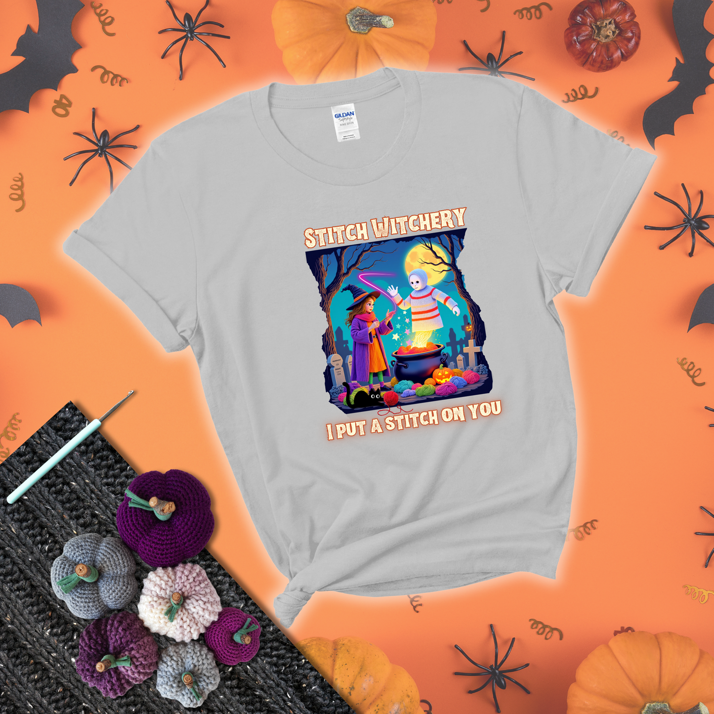 A Halloween scene with a young witch casting a yarn spell from a cauldron onto a floating crochet-ghost figure, under the phrase “I Put a Stitch on You” showing a light grey tee with a festive Halloween background
