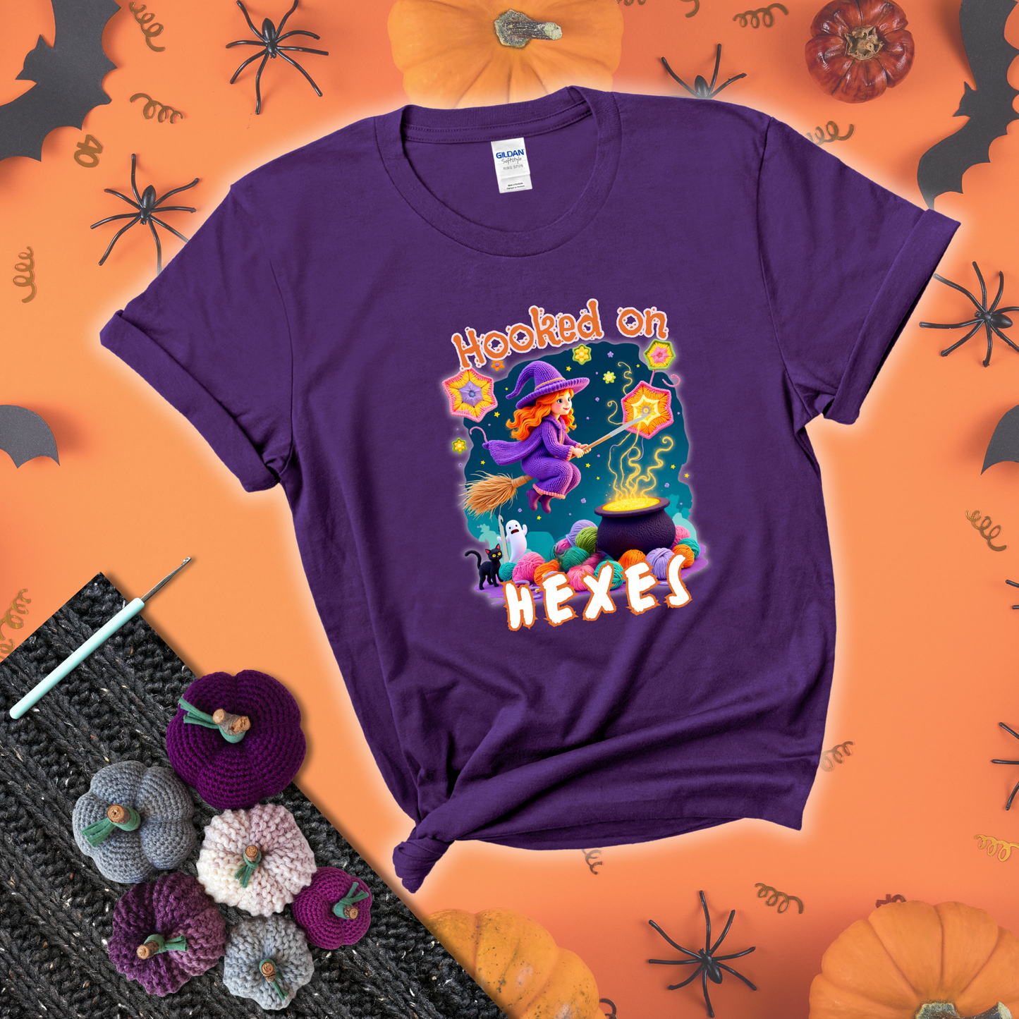 Witchy vibe with stars, hexagons, and a crochet hook. Text reads: “Hooked on Hexes.” A mystical and moody tee for fans of spooky stitches showing a purple tee with a festive Halloween background