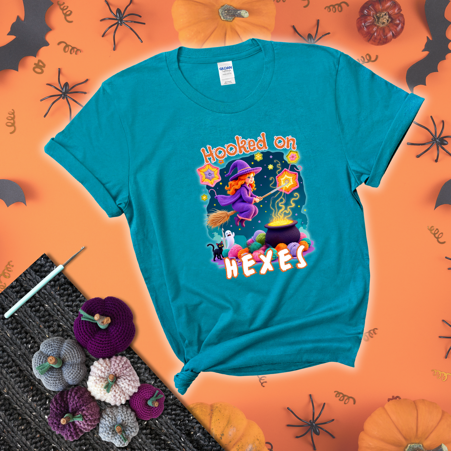 Witchy vibe with stars, hexagons, and a crochet hook. Text reads: “Hooked on Hexes.” A mystical and moody tee for fans of spooky stitches showing a blue-green tee with a festive Halloween background