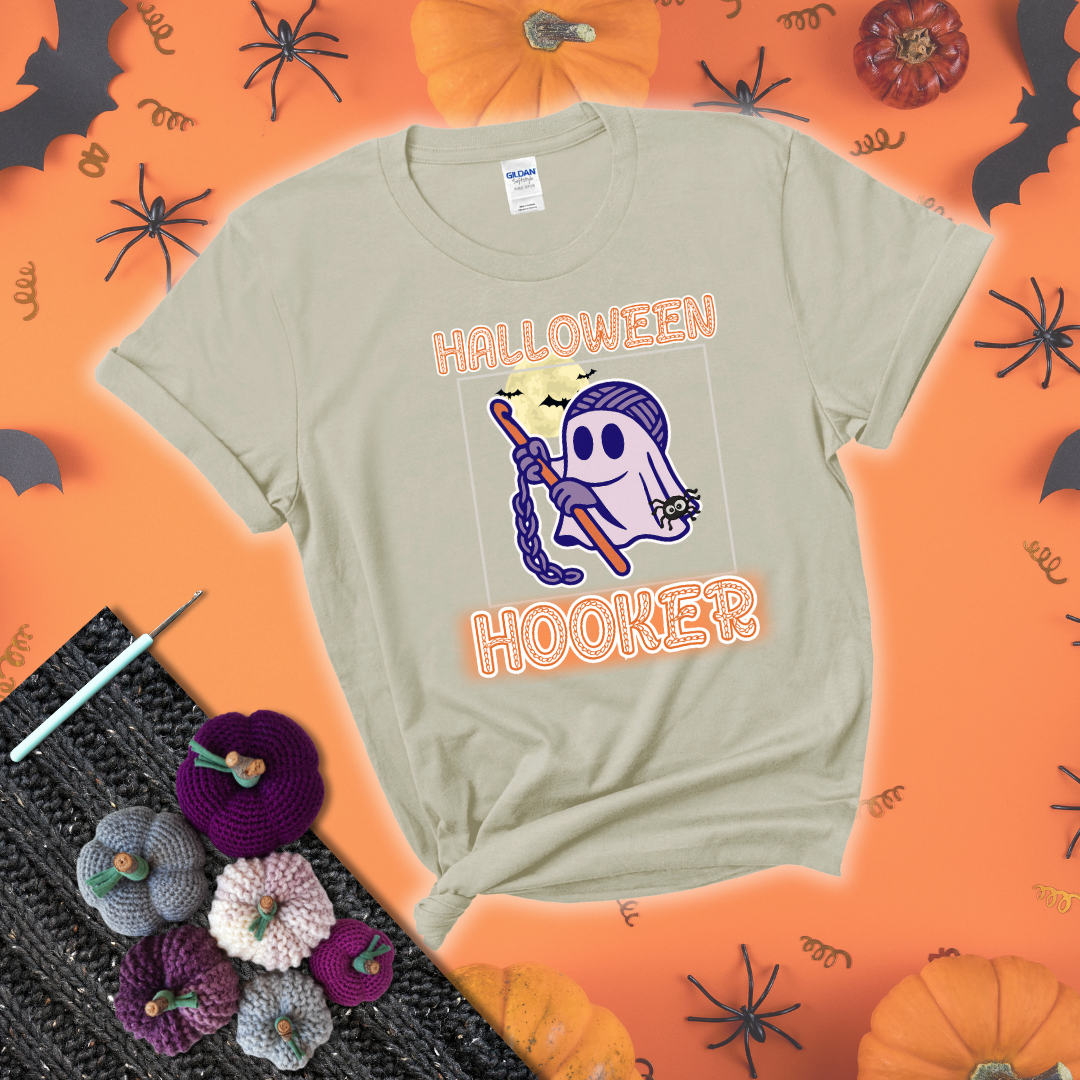 Cartoon ghost crocheter with a yarn ball head, crochet hook, bats, and text “Halloween Hooker,” a fun spooky tee for yarn lovers showing a beige tee with a festive Halloween background