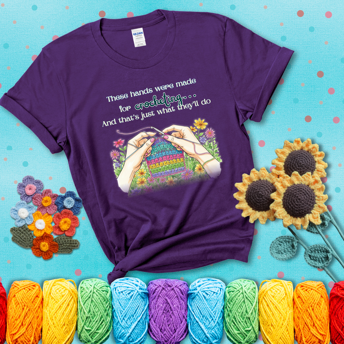 Illustration of two hands crocheting a rainbow swatch, surrounded by vibrant flowers with the phrase “These hands were made for crocheting… and that’s just what they’ll do,” showing a purple tee with a teal sunflower background