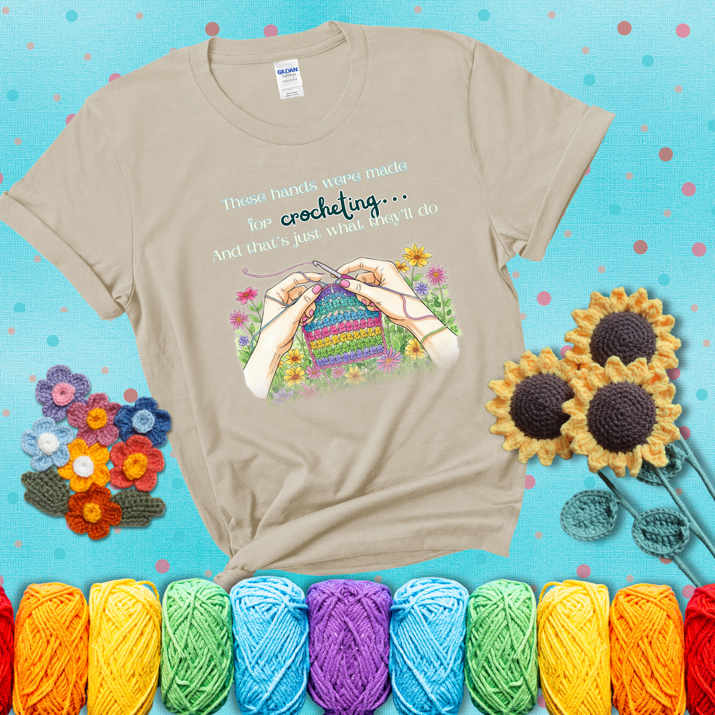 Illustration of two hands crocheting a rainbow swatch, surrounded by vibrant flowers with the phrase “These hands were made for crocheting… and that’s just what they’ll do,” showing a beige tee with a teal sunflower background