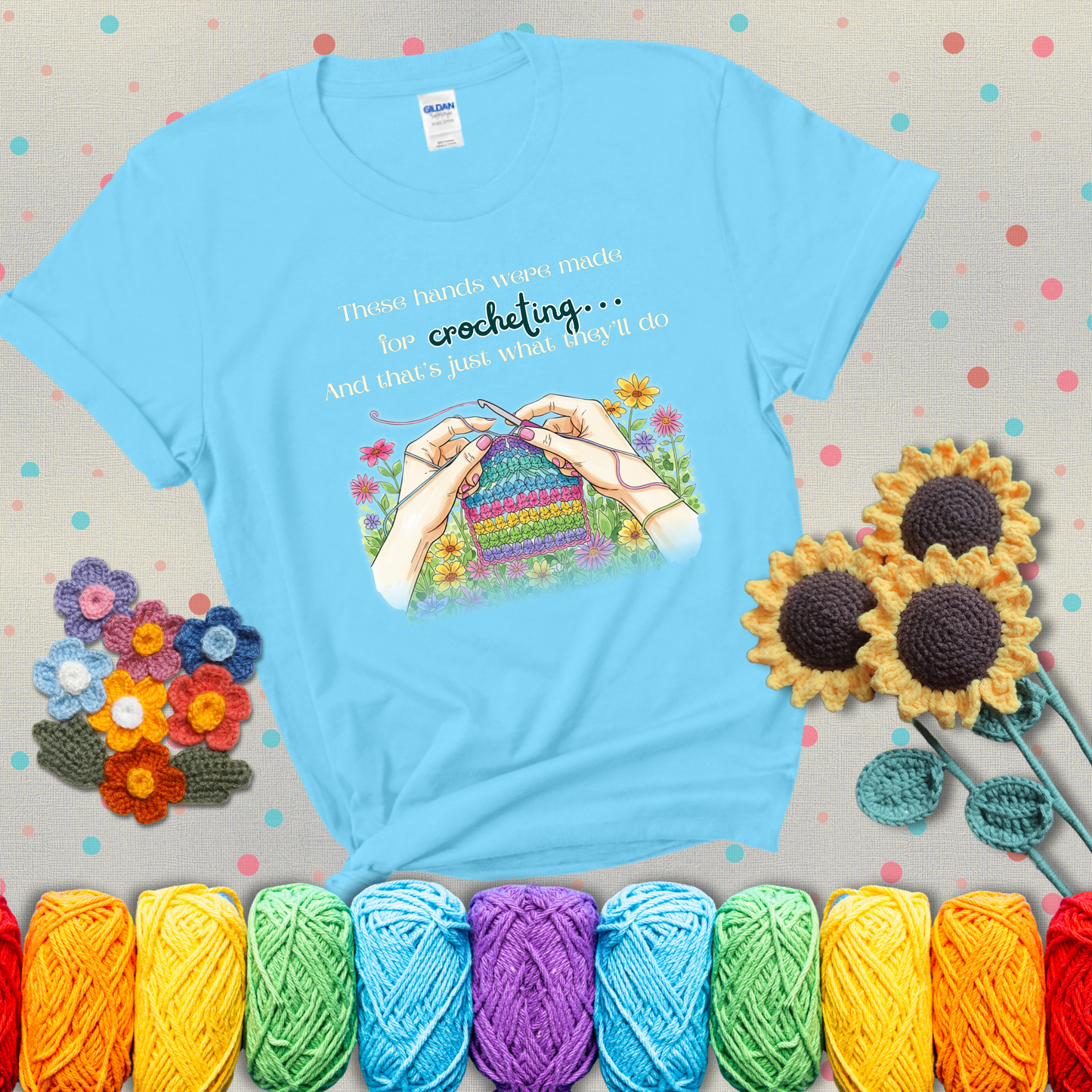 Illustration of two hands crocheting a rainbow swatch, surrounded by vibrant flowers with the phrase “These hands were made for crocheting… and that’s just what they’ll do,” showing a light blue tee with grey sunflower background