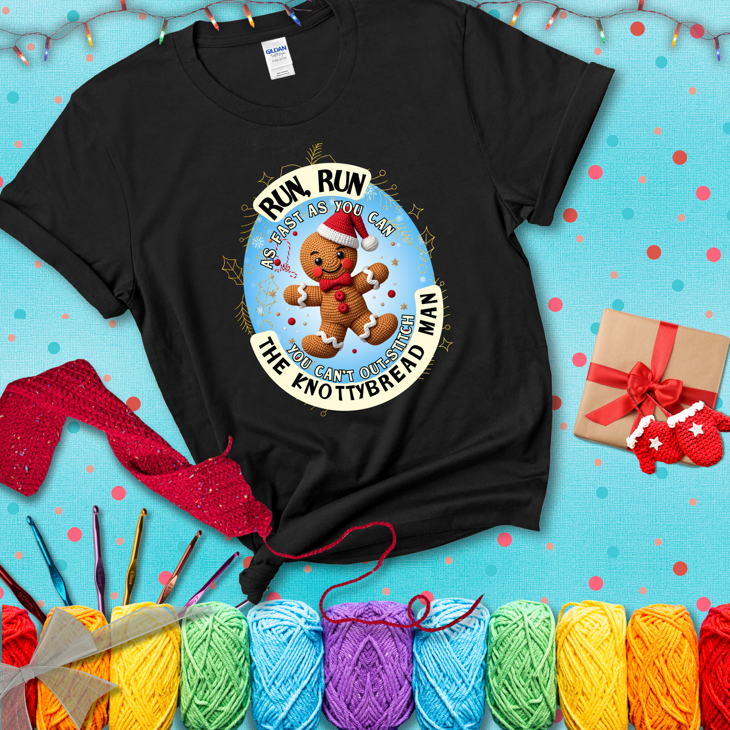 Cute crocheted gingerbread man in Santa hat with playful text: “Run, Run As Fast As You Can, You Can’t Out-Stitch the Knottybread Man.” A festive crochet pun shirt, showing a black tee with a festive Christmas background