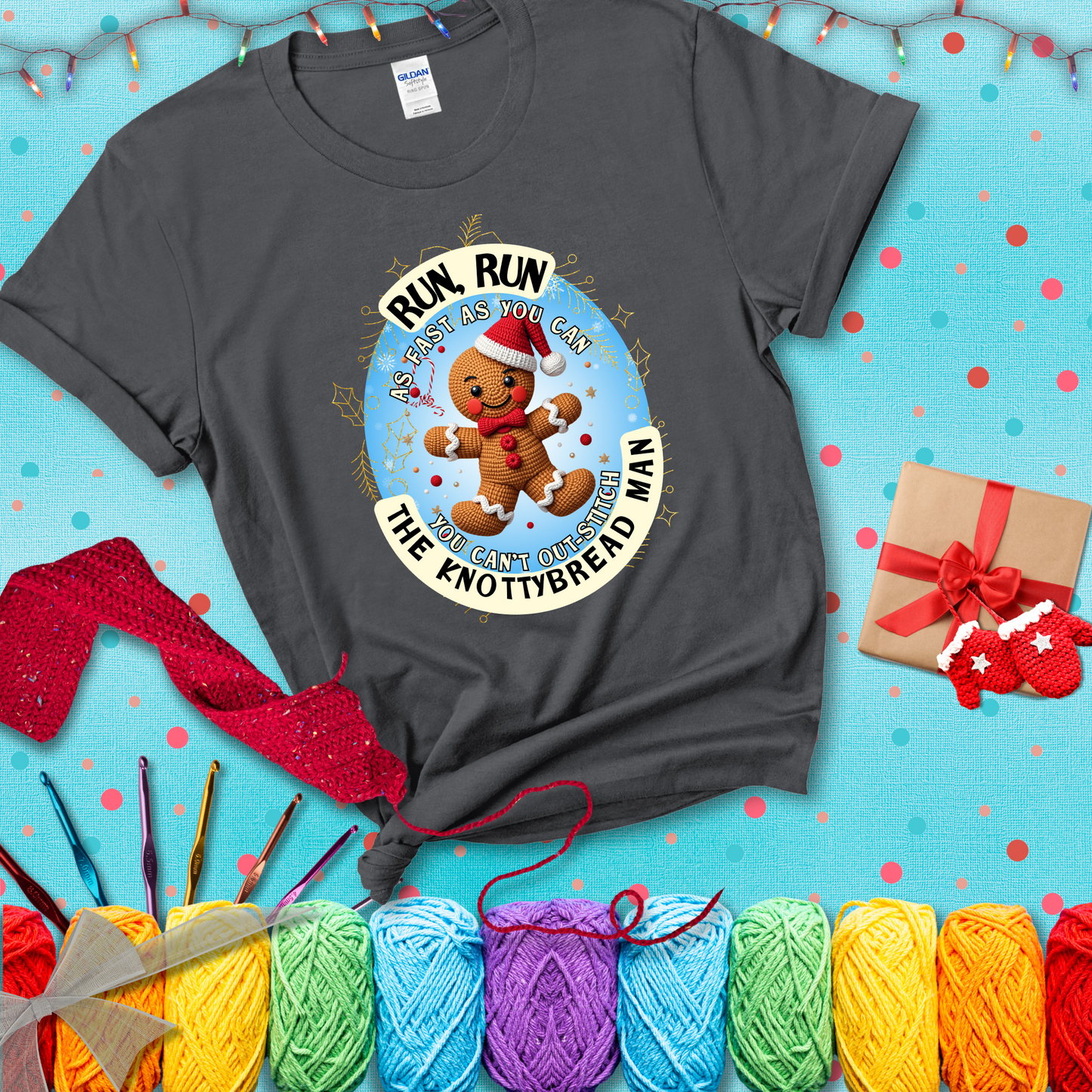 Cute crocheted gingerbread man in Santa hat with playful text: “Run, Run As Fast As You Can, You Can’t Out-Stitch the Knottybread Man.” A festive crochet pun shirt, showing a dark grey tee with a festive Christmas background