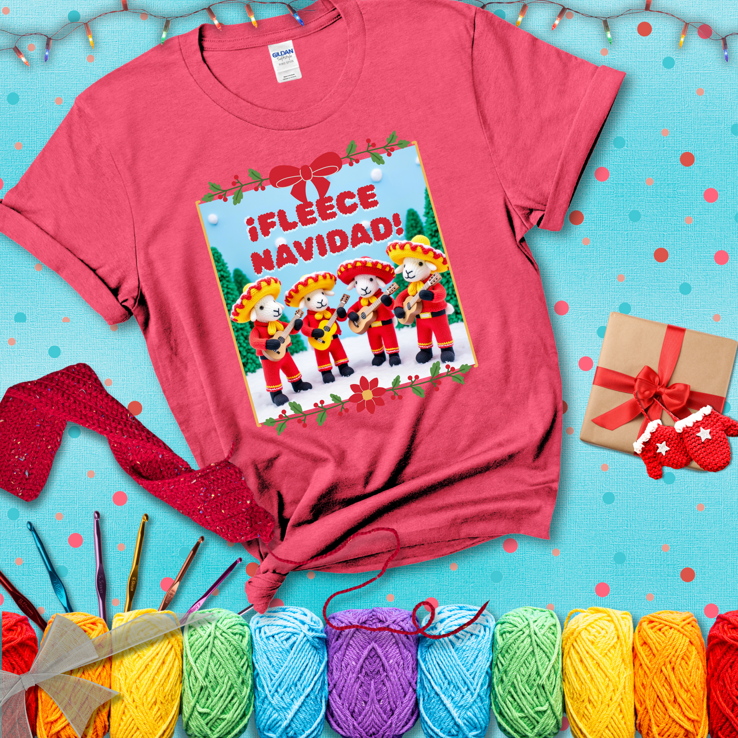 Four crocheted sheep dressed in red mariachi outfits with guitars, standing in a snowy scene under the phrase “¡Fleece Navidad!” showing a light red tee with a festive Christmas background