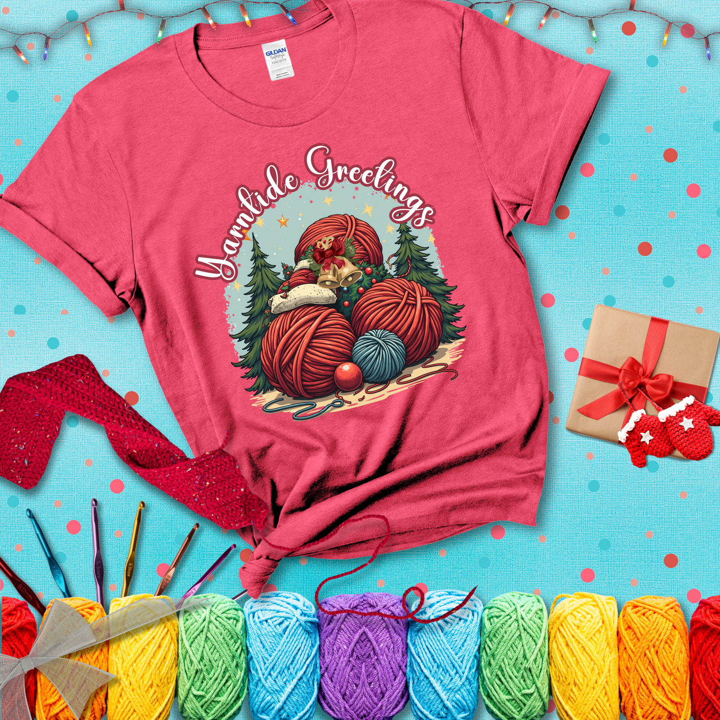 Pile of colorful yarn balls with bells, bows, and trees, with the phrase “Yarntide Greetings.” Cozy and festive holiday crochet tee, showing a light red tee with a festive Christmas background