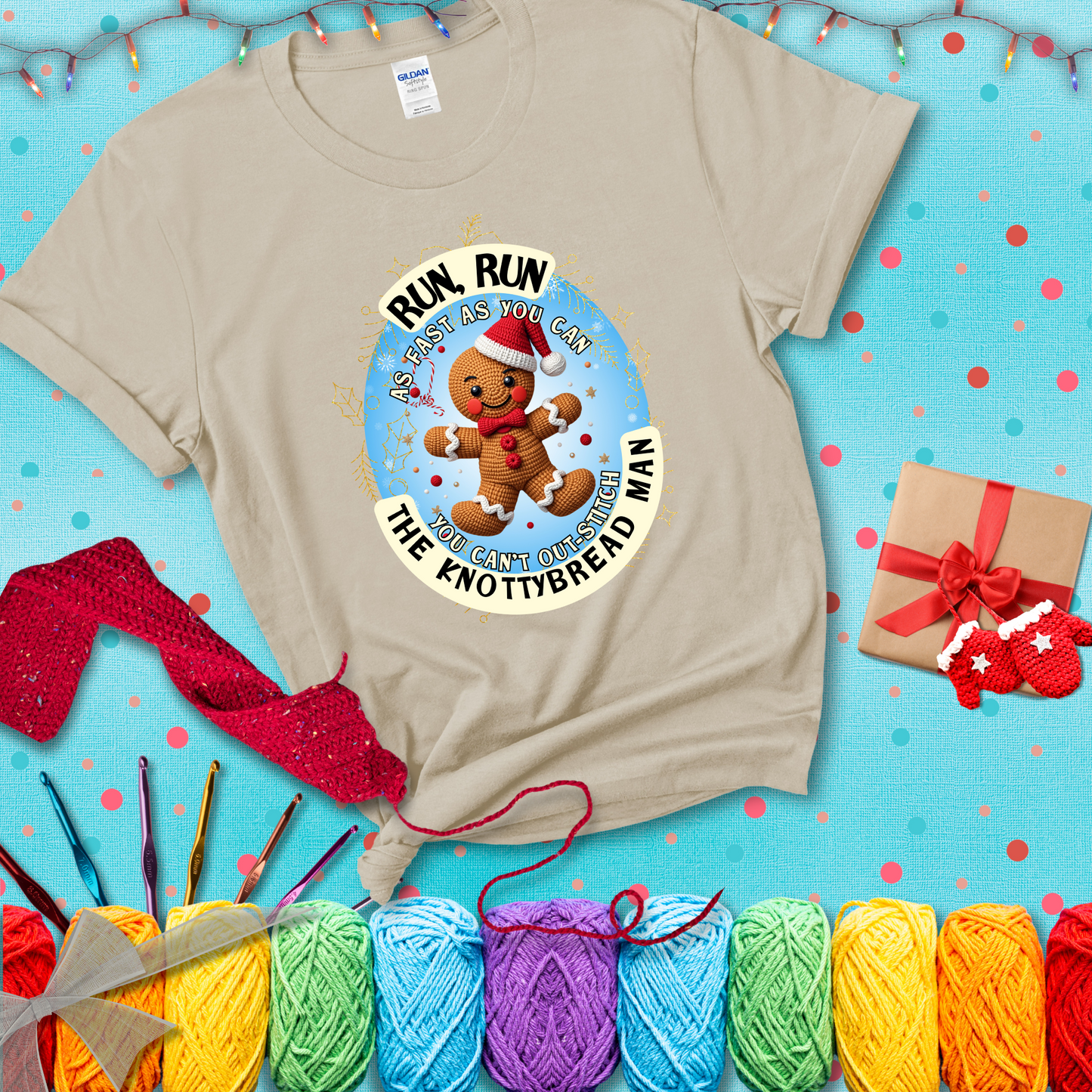 Cute crocheted gingerbread man in Santa hat with playful text: “Run, Run As Fast As You Can, You Can’t Out-Stitch the Knottybread Man.” A festive crochet pun shirt, showing a beige tee with a festive Christmas background