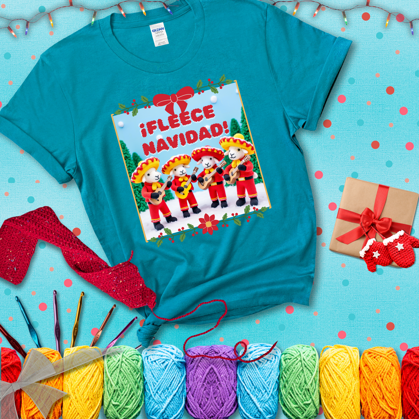 Four crocheted sheep dressed in red mariachi outfits with guitars, standing in a snowy scene under the phrase “¡Fleece Navidad!” showing a blue-green tee with a festive Christmas background