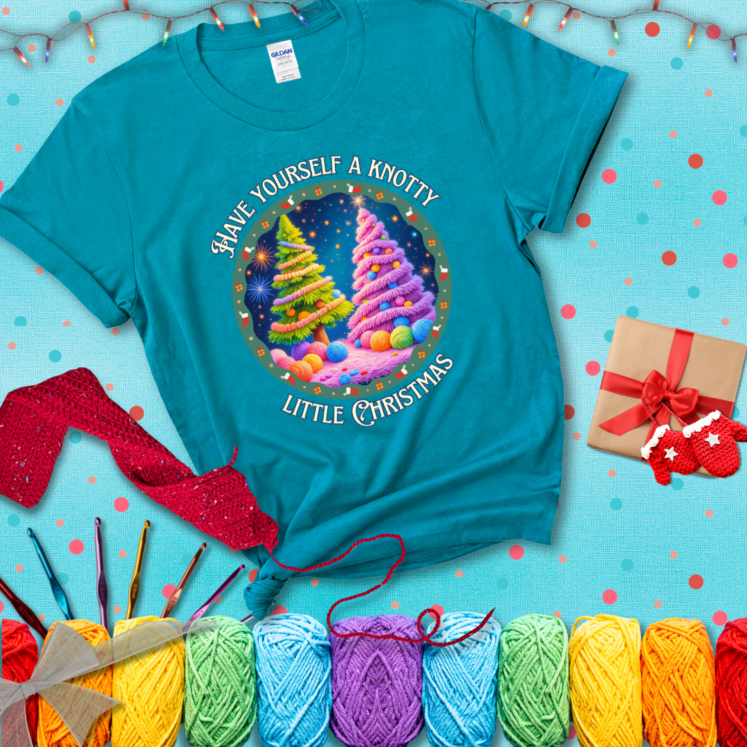 Two yarn-covered Christmas trees wrapped in colorful strands of yarn, with the phrase "Have Yourself a Knotty Little Christmas" encircling the scene showing a blue-green tee with a festive Christmas background