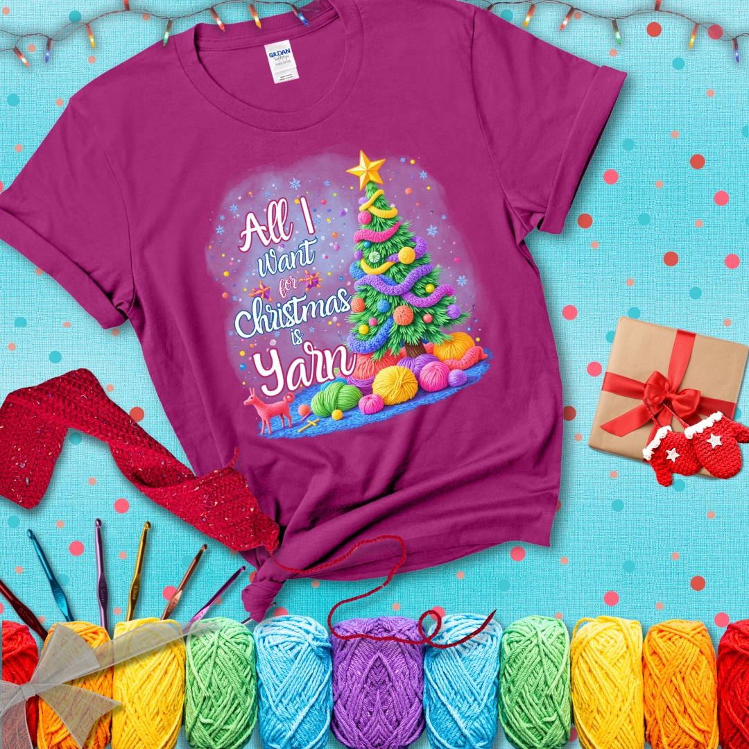 Bright Christmas tree decorated with yarn garlands, balls of yarn underneath, and the text “All I Want for Christmas is Yarn” in festive fonts, showing a magenta tee with a festive Christmas background