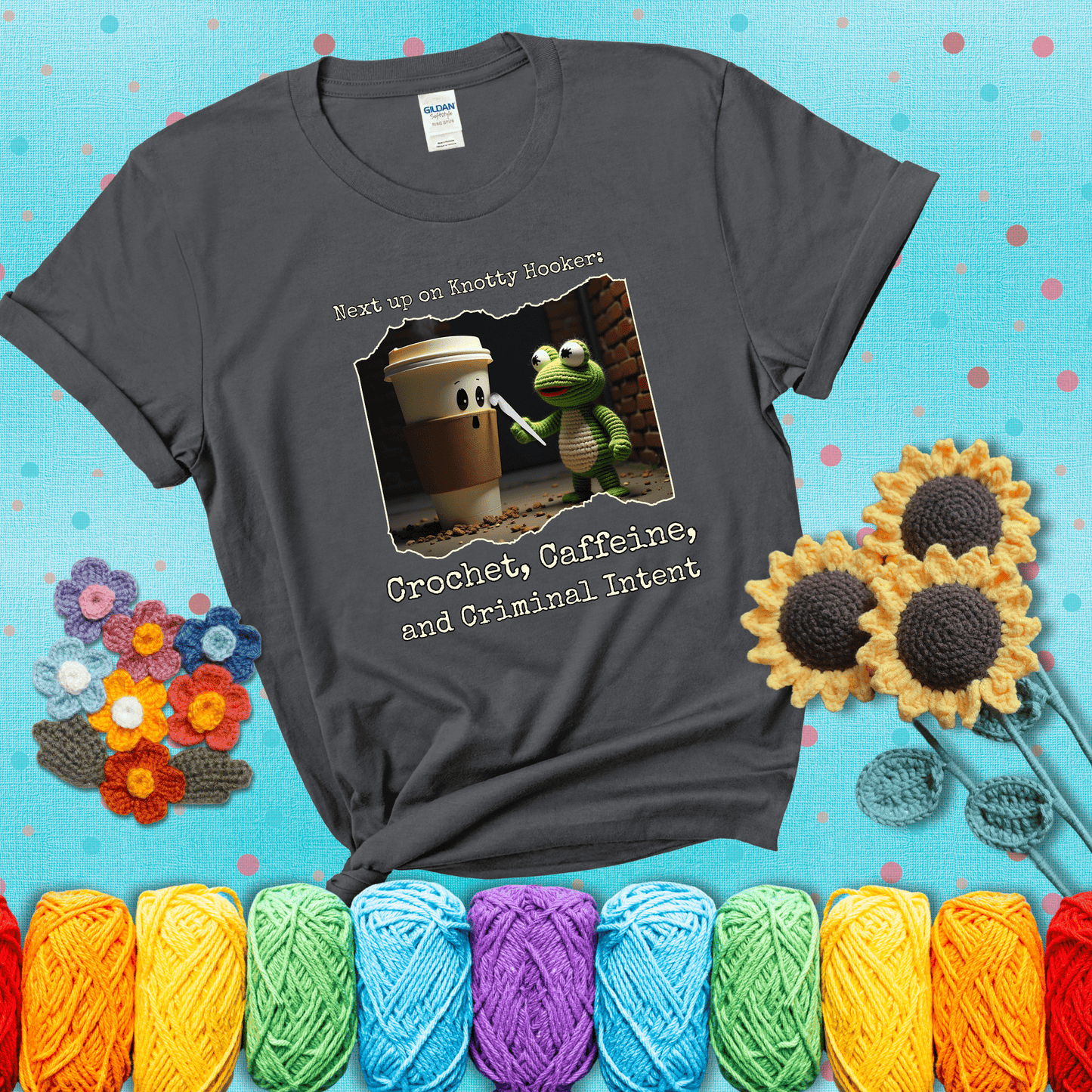 A crocheted frog holding a crochet hook confronts a surprised coffee cup in a dim alleyway with text: "Next up on Knotty Hooker: Crochet, Caffeine, and Criminal Intent," showing a dark grey tee with a teal sunflower background