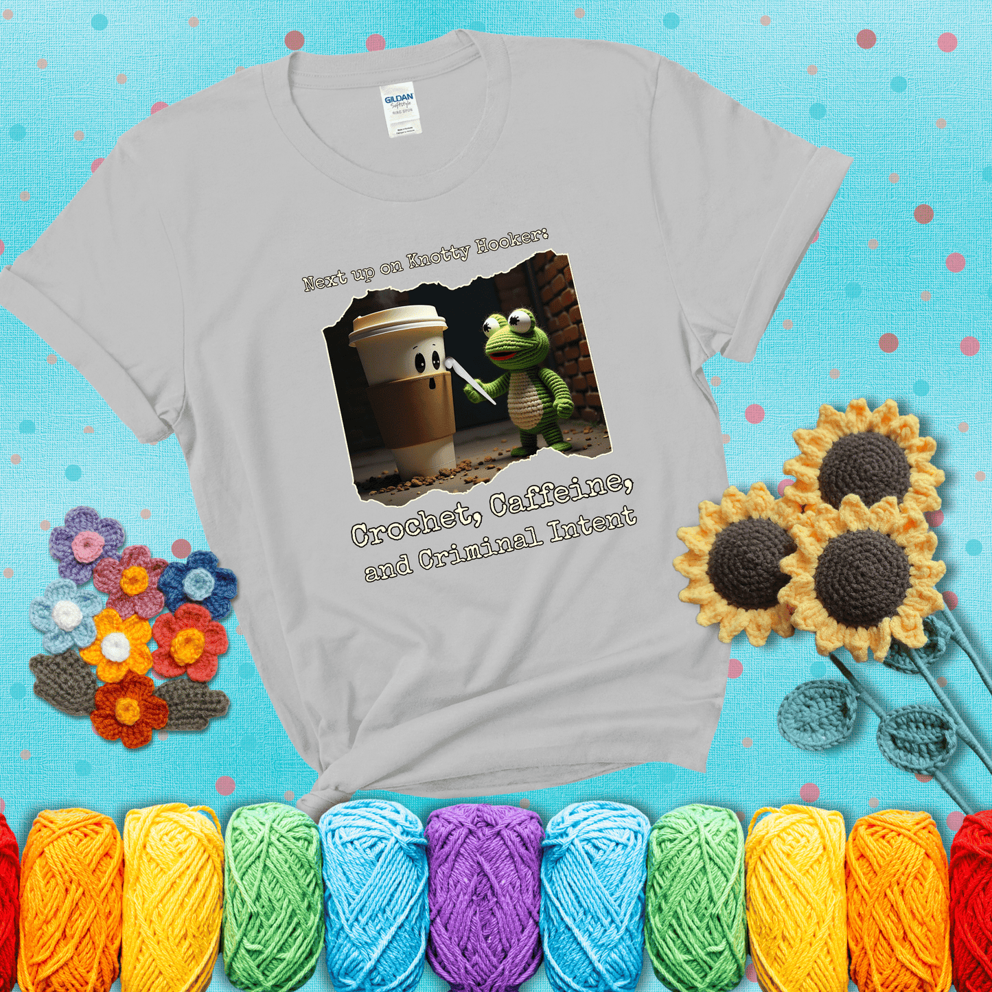 A crocheted frog holding a crochet hook confronts a surprised coffee cup in a dim alleyway with text: "Next up on Knotty Hooker: Crochet, Caffeine, and Criminal Intent," showing a light grey tee with a teal sunflower background