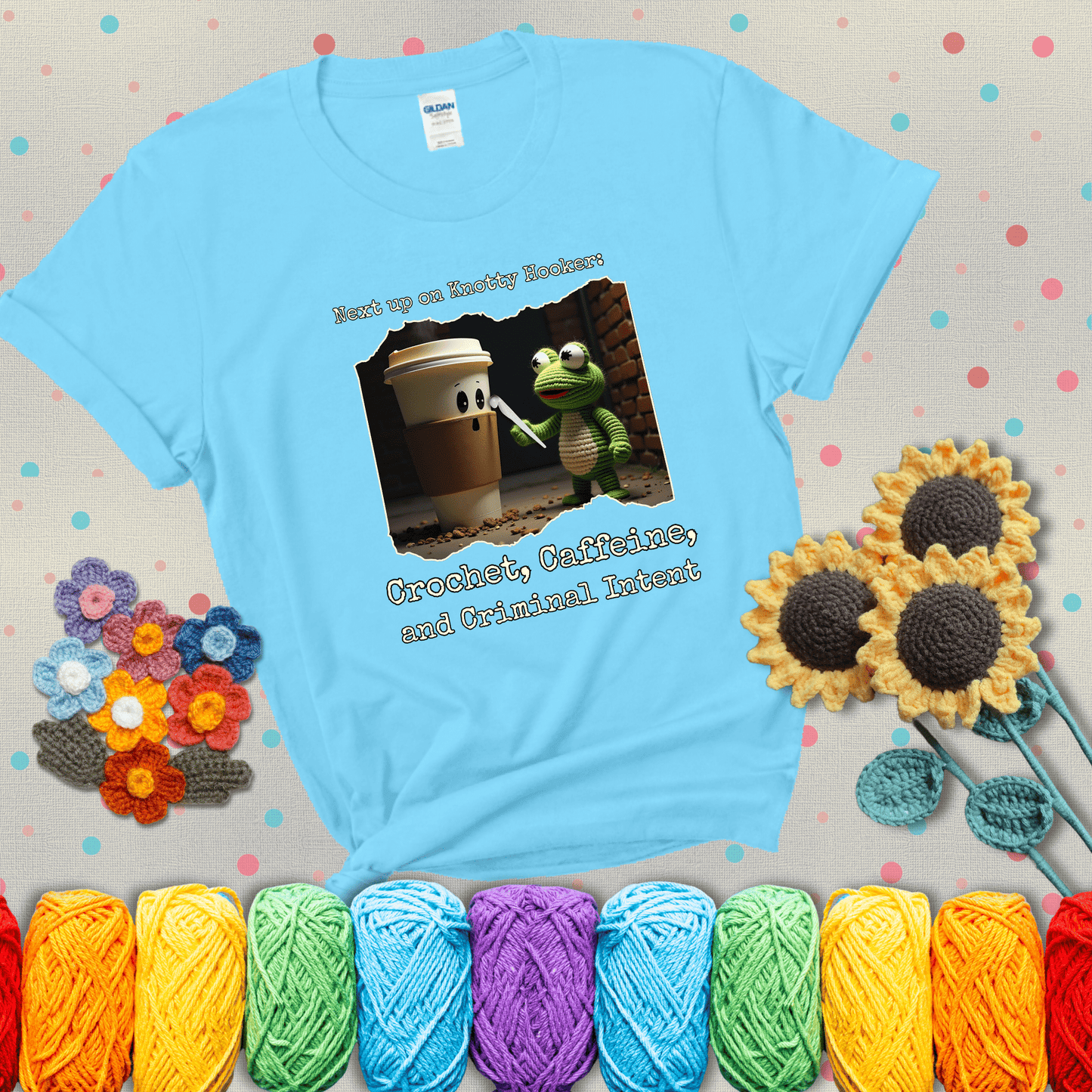 A crocheted frog holding a crochet hook confronts a surprised coffee cup in a dim alleyway with text: "Next up on Knotty Hooker: Crochet, Caffeine, and Criminal Intent," showing a light blue tee with grey sunflower background