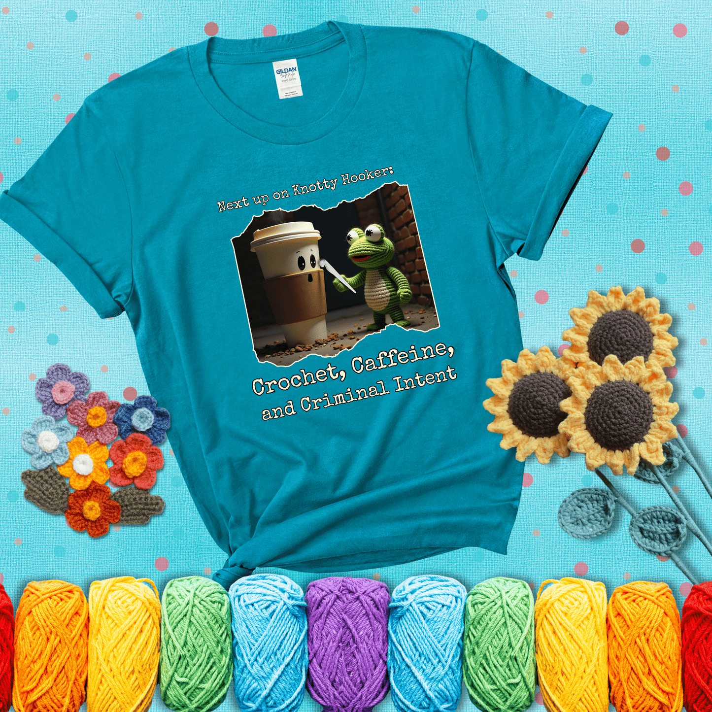 A crocheted frog holding a crochet hook confronts a surprised coffee cup in a dim alleyway with text: "Next up on Knotty Hooker: Crochet, Caffeine, and Criminal Intent," showing a blue-green tee with a teal sunflower background