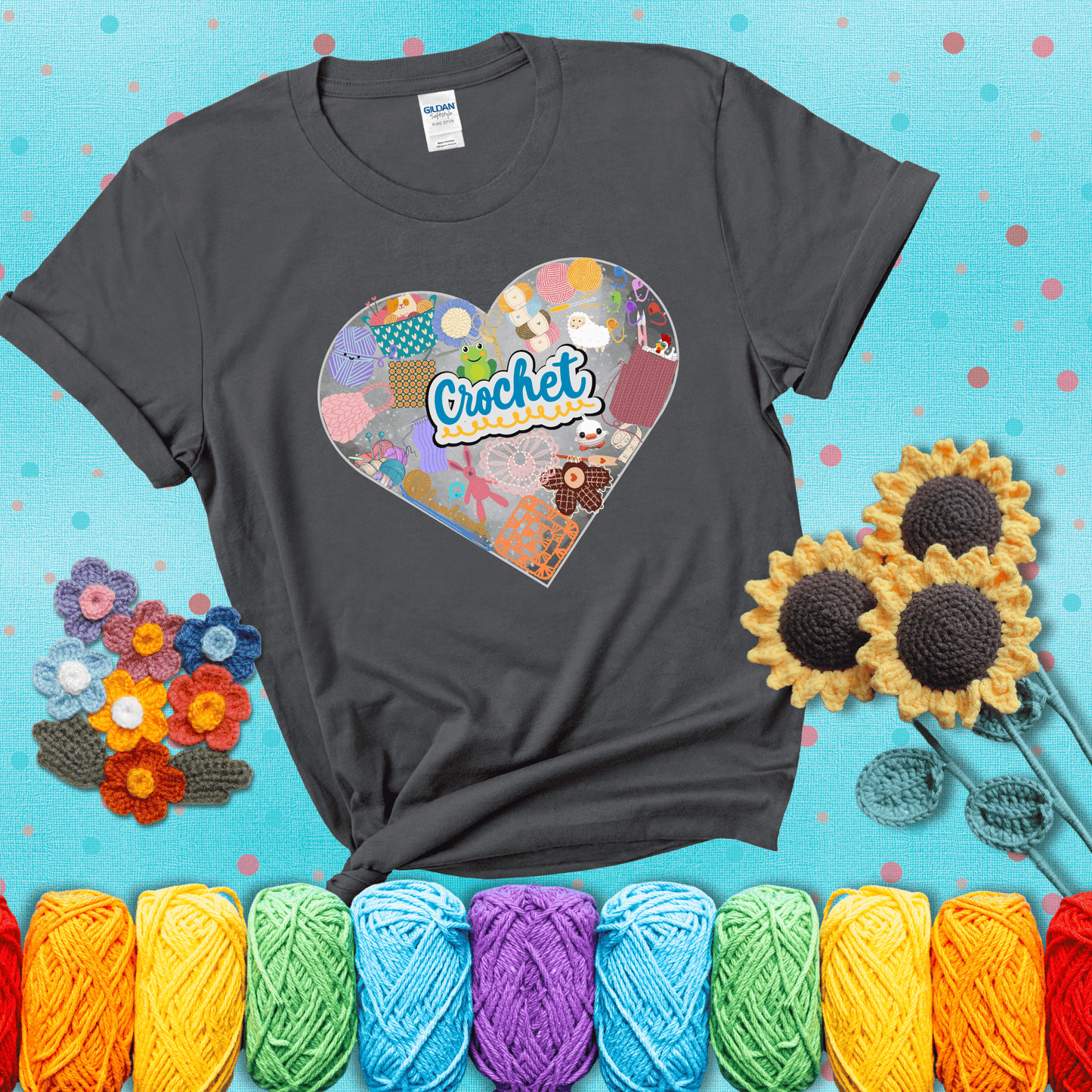 A heart filled with colorful crochet essentials including yarn, hooks, scissors, notions, and handmade items, with the word "Crochet" prominently in the center, showing a dark grey tee with a teal sunflower background