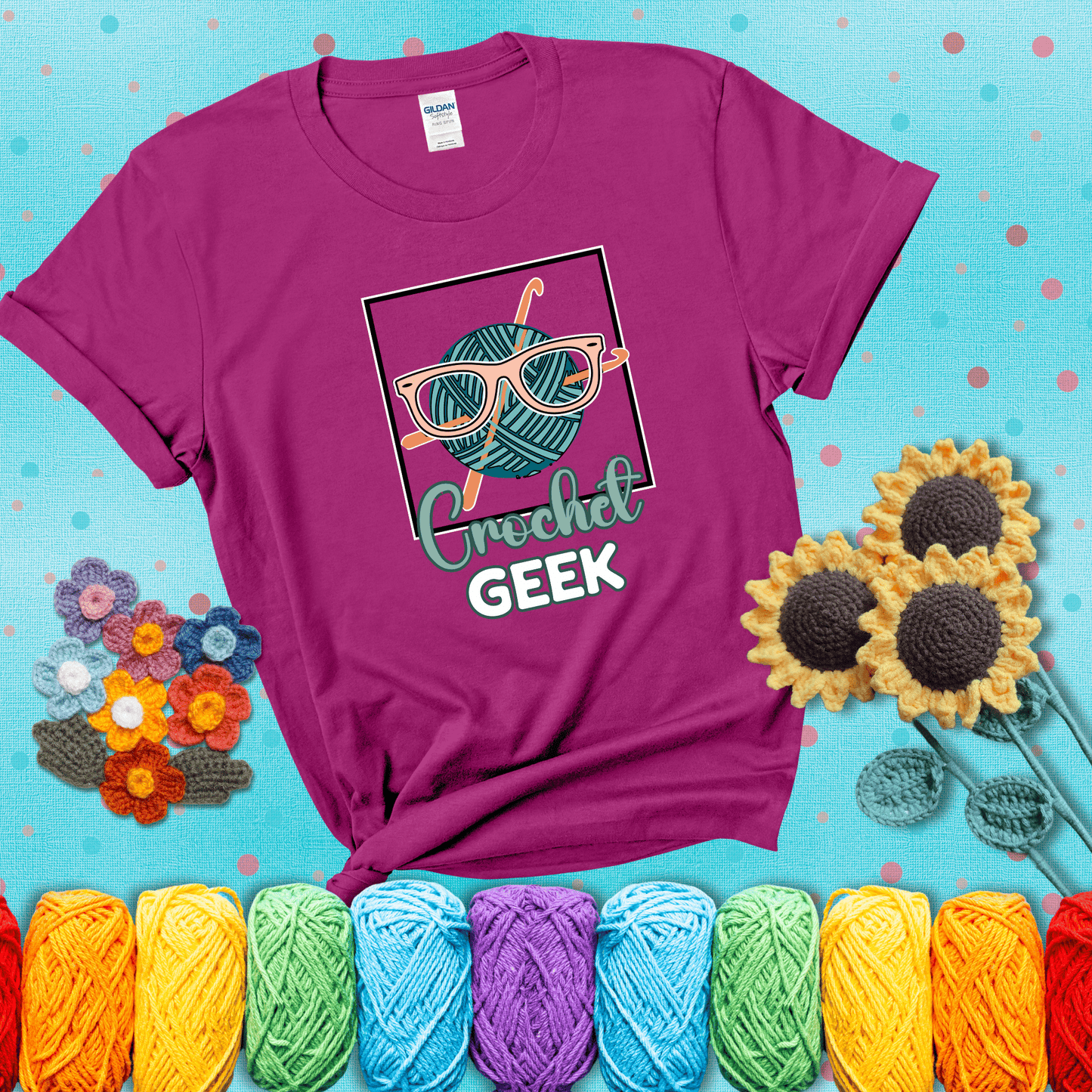 A teal yarn ball with crisscrossed hooks wears oversized nerdy glasses with the phrase “Crochet Geek” in bold, fun text below, showing a magenta tee with a teal sunflower background