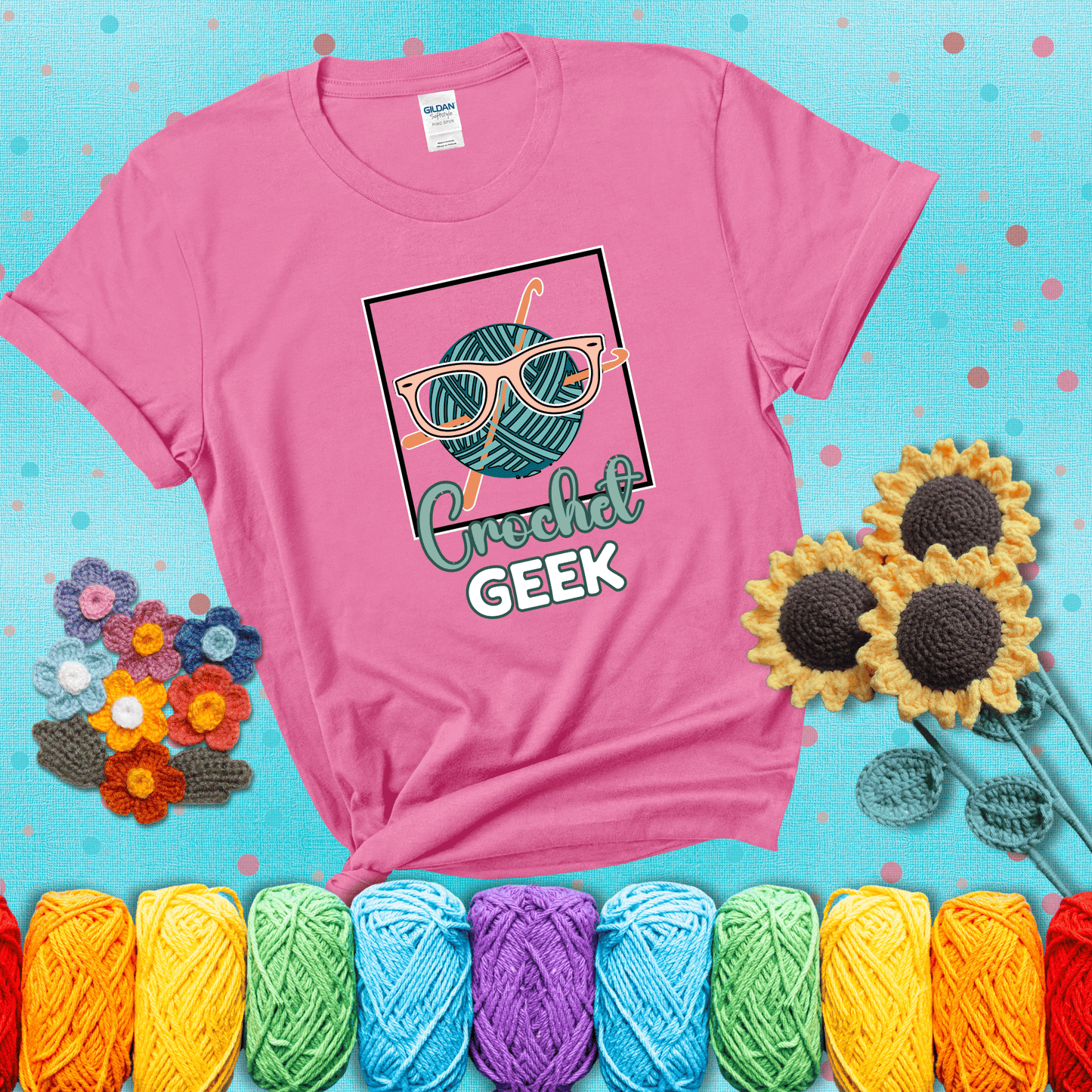 A teal yarn ball with crisscrossed hooks wears oversized nerdy glasses with the phrase “Crochet Geek” in bold, fun text below, showing a pink tee with a teal sunflower background