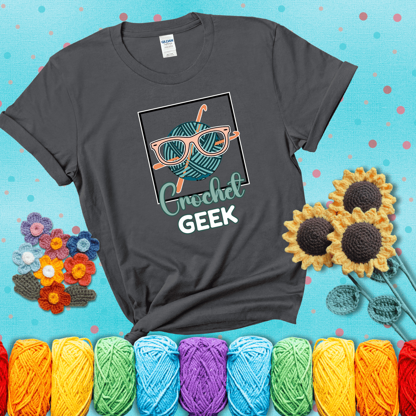 A teal yarn ball with crisscrossed hooks wears oversized nerdy glasses with the phrase “Crochet Geek” in bold, fun text below, showing a dark grey tee with a teal sunflower background