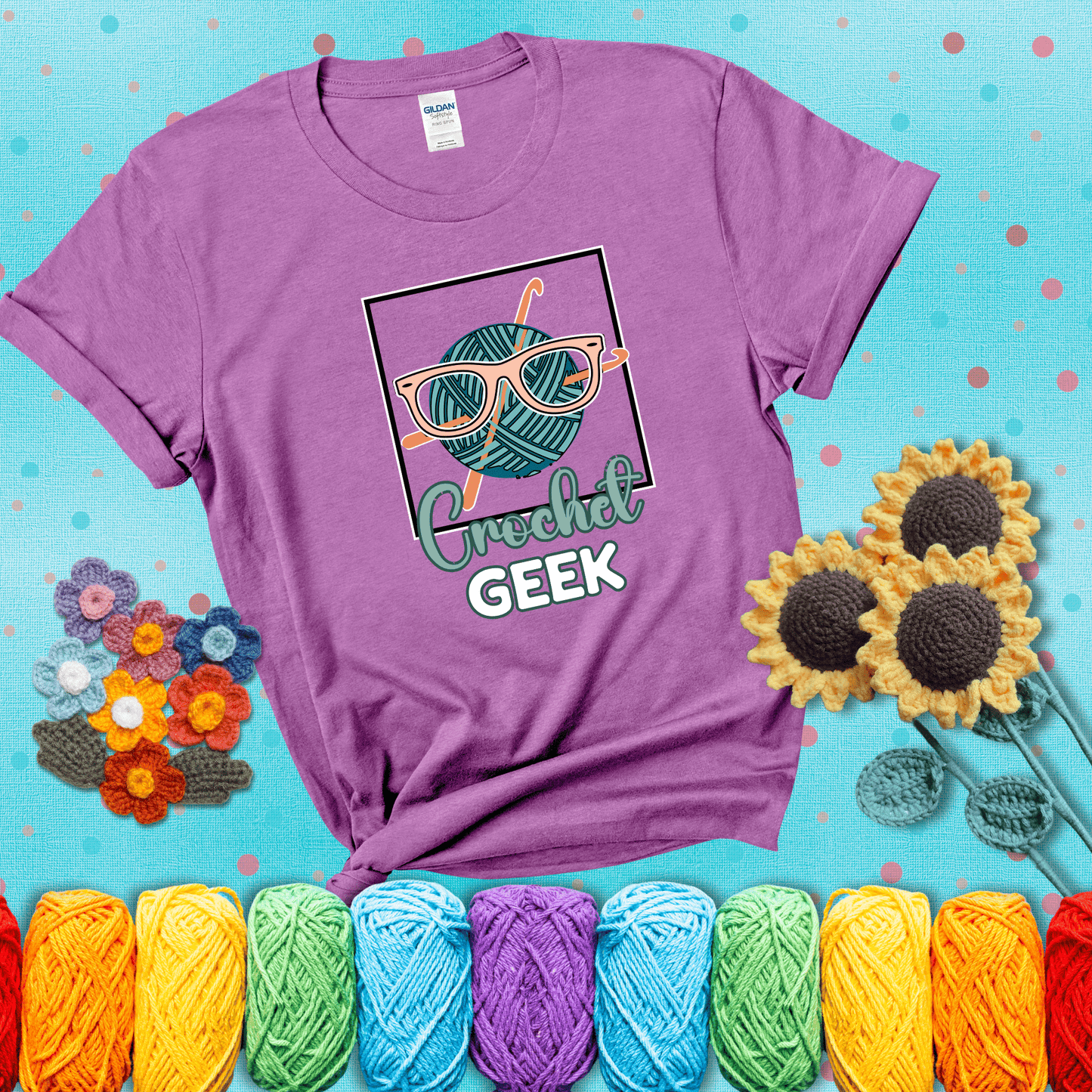 A teal yarn ball with crisscrossed hooks wears oversized nerdy glasses with the phrase “Crochet Geek” in bold, fun text below, showing a light purple tee with a teal sunflower background