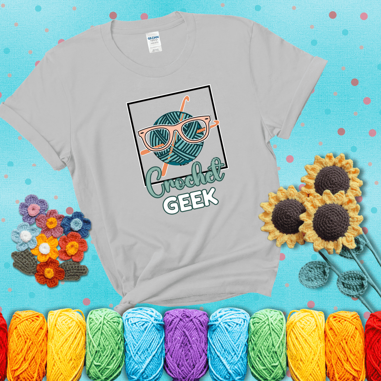 A teal yarn ball with crisscrossed hooks wears oversized nerdy glasses with the phrase “Crochet Geek” in bold, fun text below, showing a light grey tee with a teal sunflower background