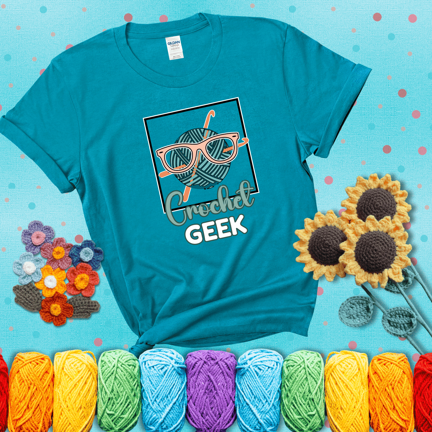 A teal yarn ball with crisscrossed hooks wears oversized nerdy glasses with the phrase “Crochet Geek” in bold, fun text below, showing a blue-green tee with a teal sunflower background