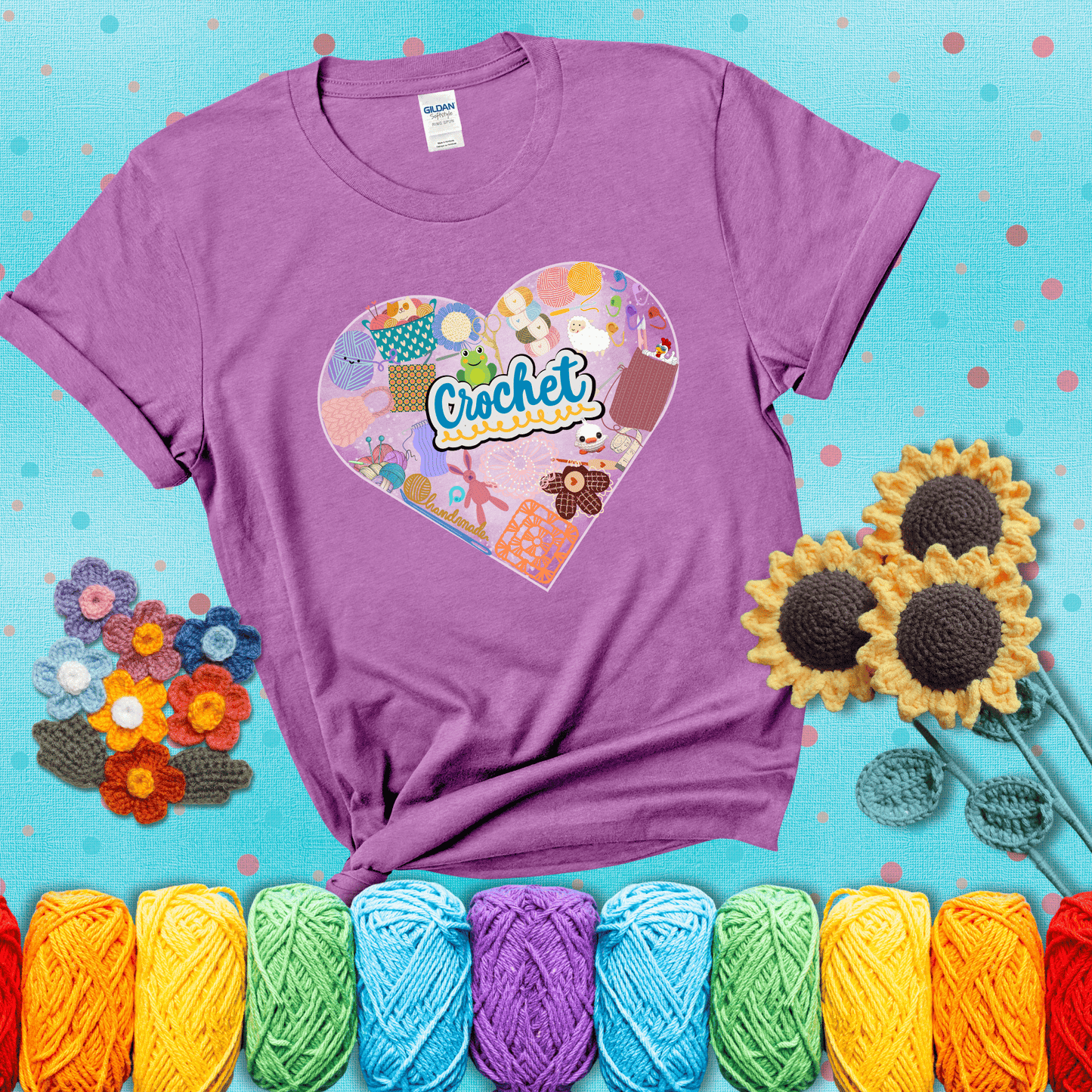 A heart filled with colorful crochet essentials including yarn, hooks, scissors, notions, and handmade items, with the word "Crochet" prominently in the center, showing a light purple tee with a teal sunflower background