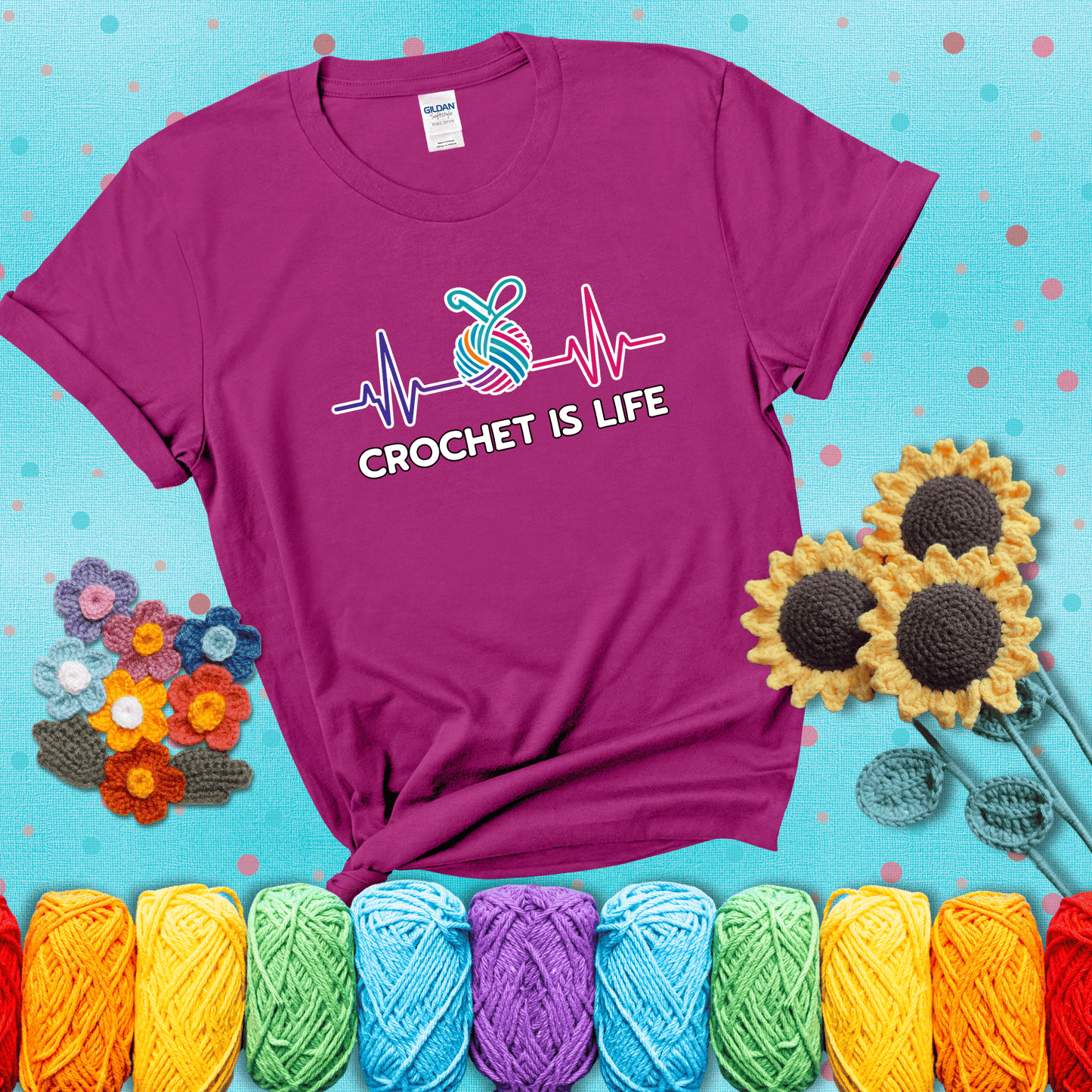 A heartbeat line with a colorful yarn ball and crochet hook in the center, with the words “Crochet is Life”, showing a magenta tee with a teal sunflower background